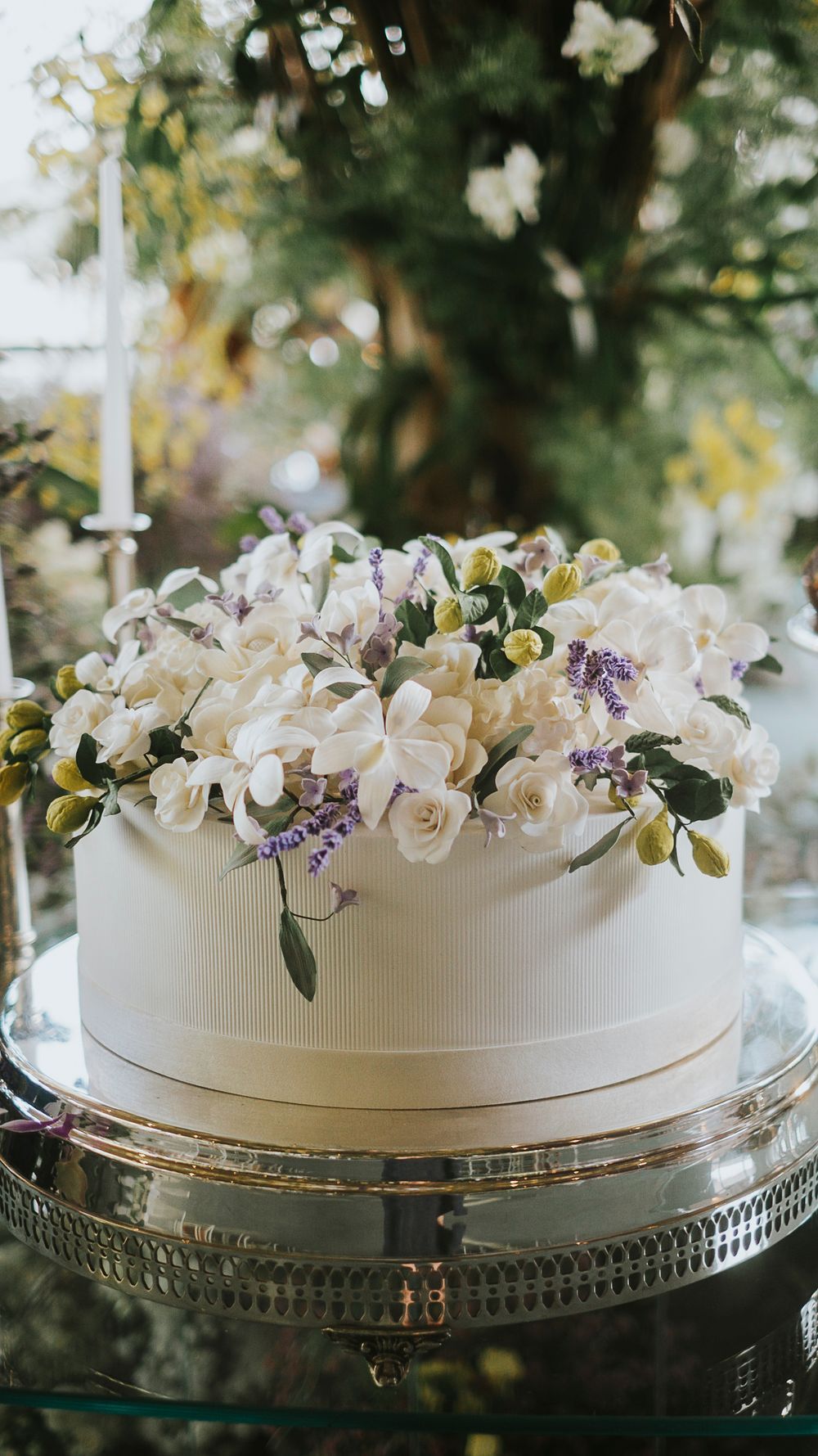 Single-tier white wedding cake topped with white orchids, roses, and purple lavender floral decorations.