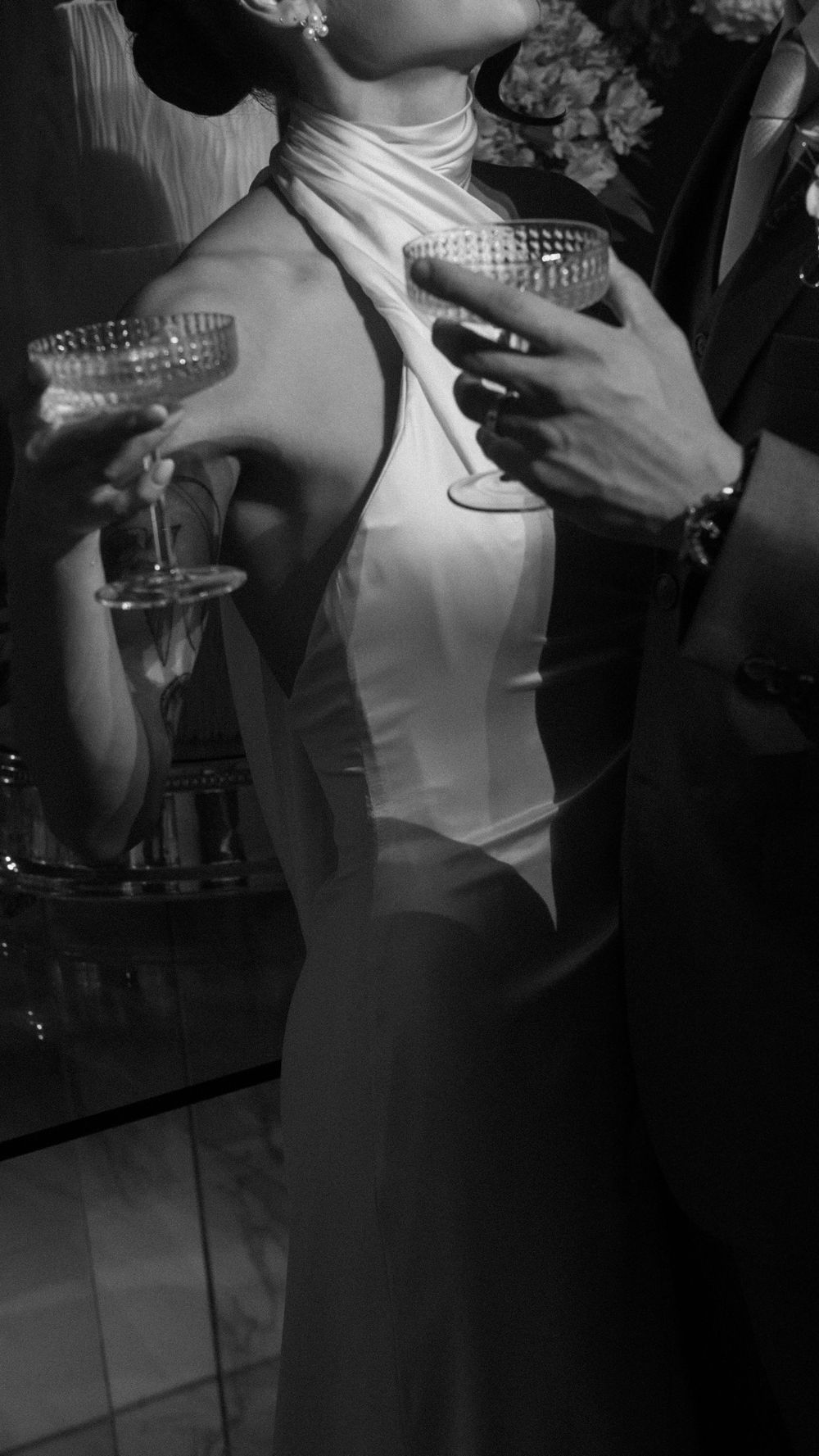 Black and white close-up of bride and groom toasting with crystal coupe glasses at their wedding reception.