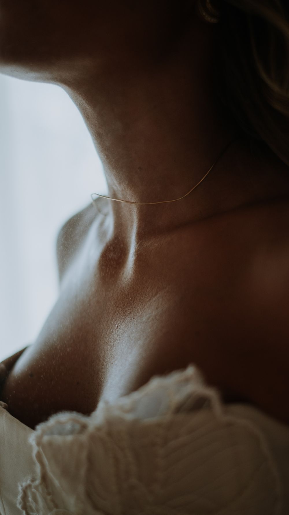 Close-up of a bride wearing a delicate gold chain necklace in soft natural light.