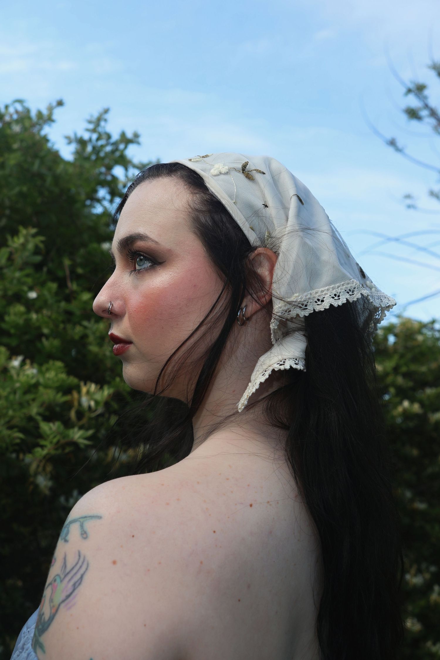 A woman wearing an embroidered bandana and off-the-shoulder blue top looking off to the left with her shoulder mostly in view.