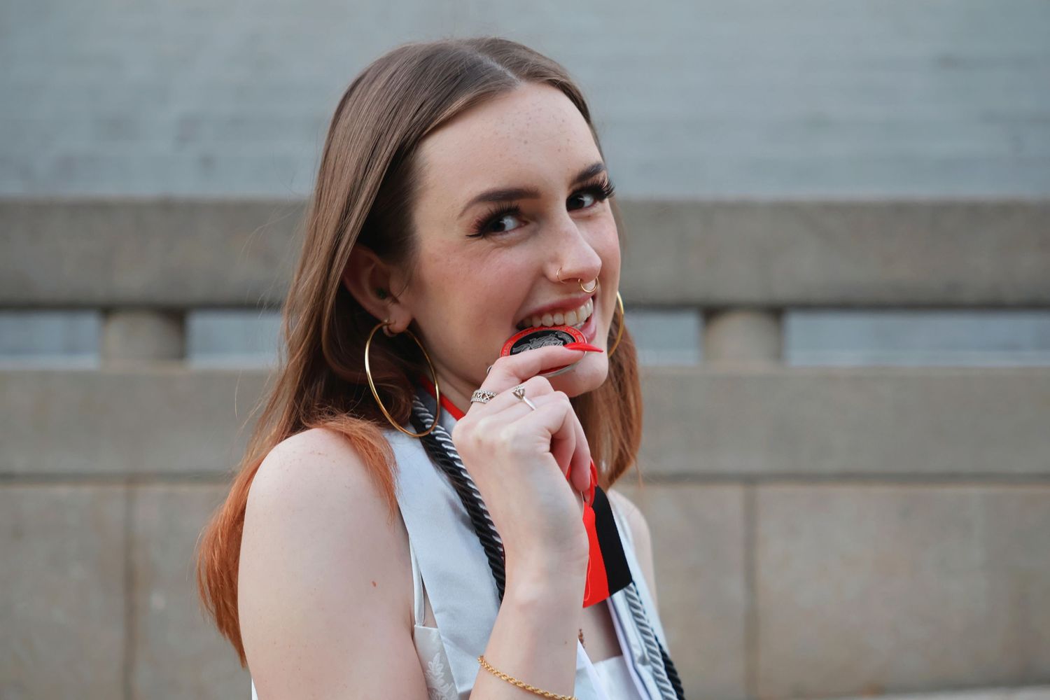 A close-up portrait of a smiling woman biting her graduation medallion while wearing her stole and honor cords.
