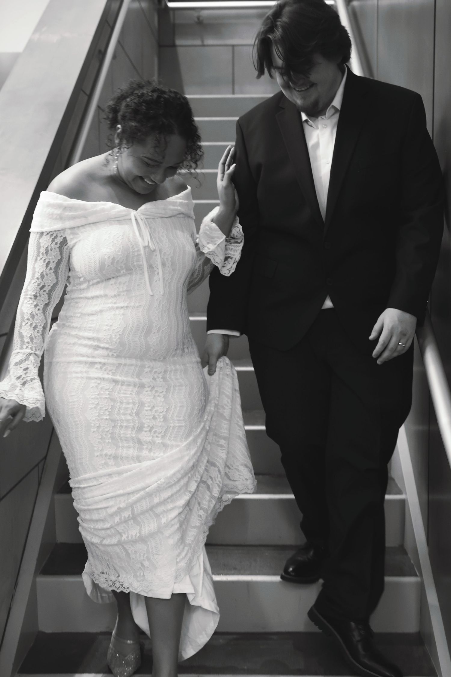 A black and white photo of a bride and groom walking down a staircase together following their wedding.