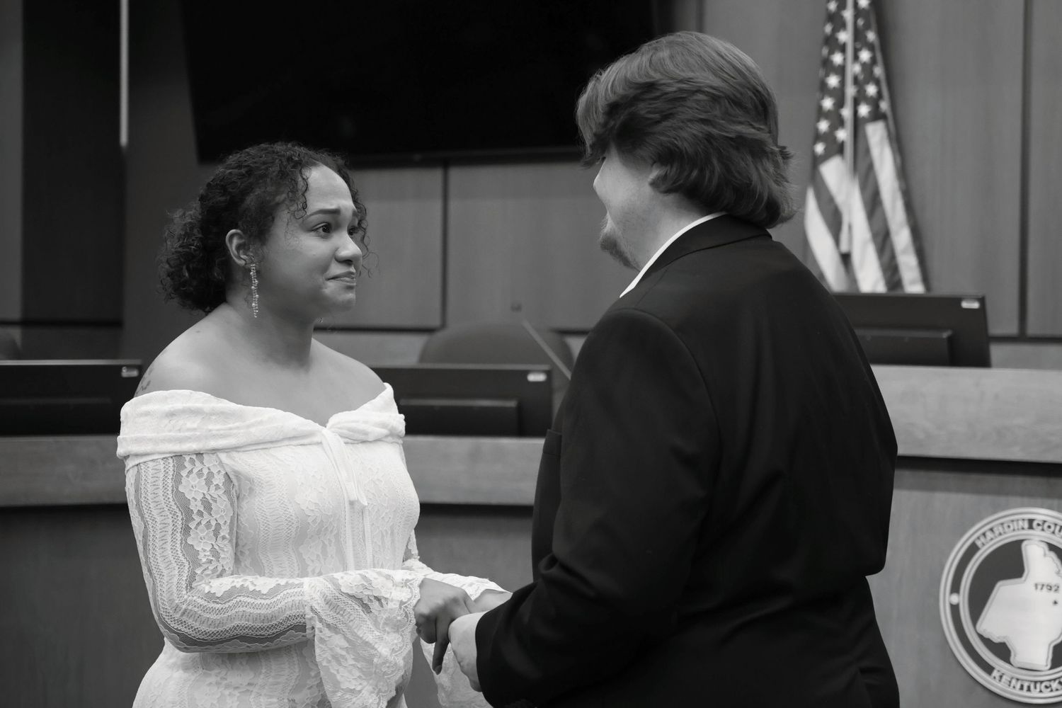 A black and white photograph of a bride and groom holding hands and exchanging vows inside a courtroom.