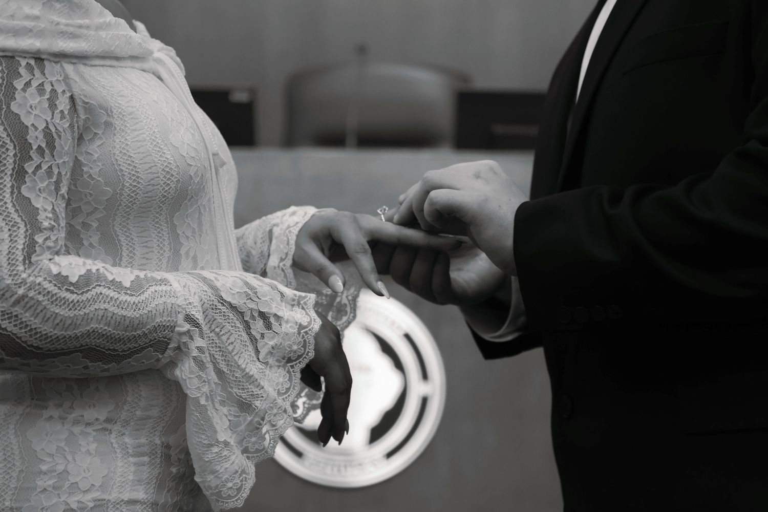 A black and white close-up shot of a groom placing a wedding band on the bride's finger during a ceremony.