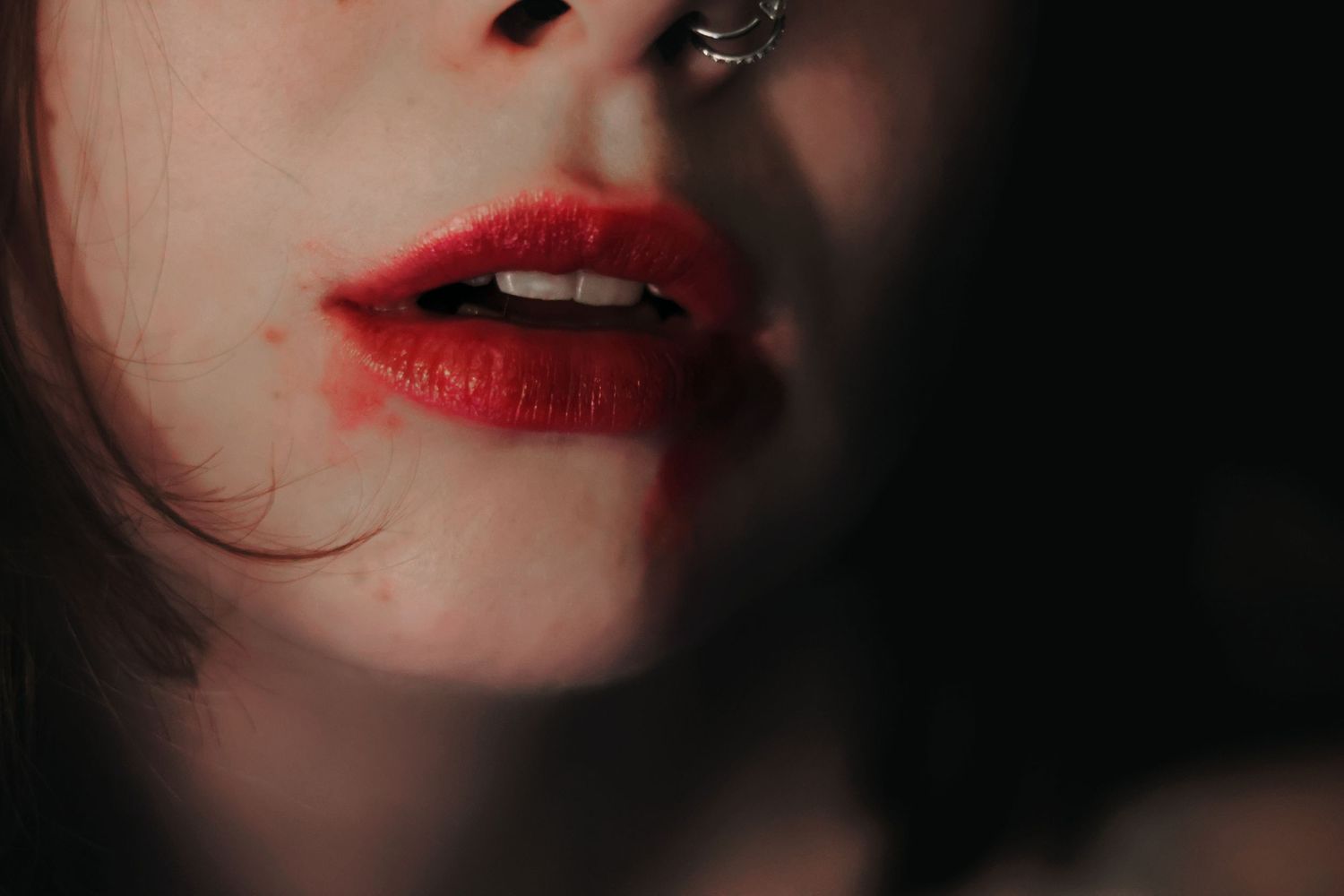 A close-up of a person's slightly open mouth featuring bright red lipstick smudged across their chin.