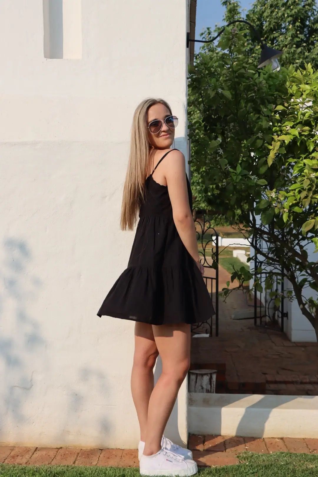 Girl standing by a white wall with sunglasses and a black dress