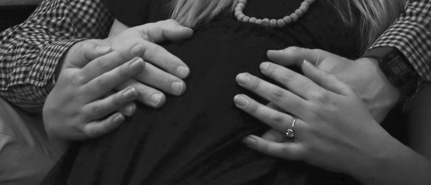 Black and white image of a couple holding a baby bump