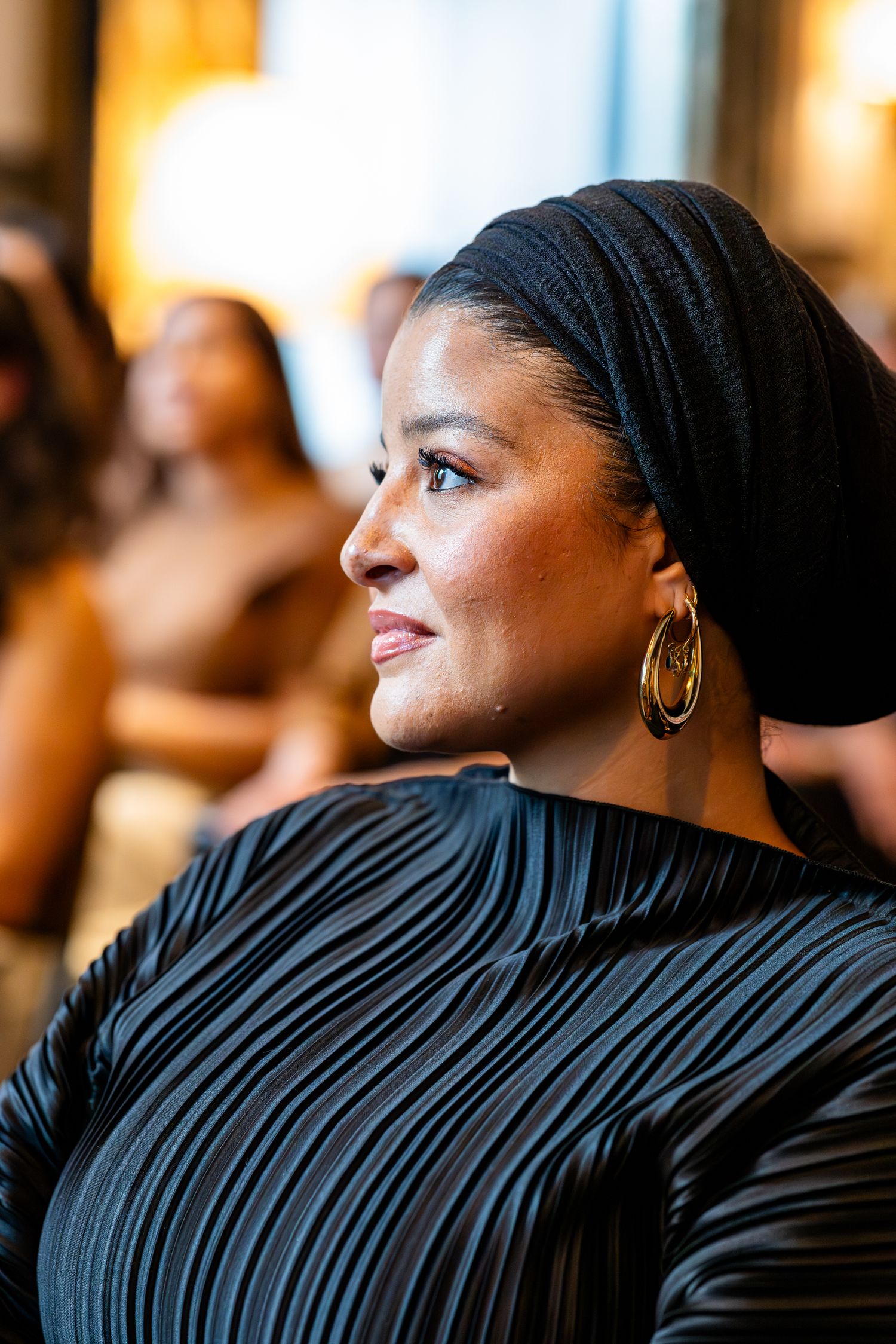 Profile view of Mooi Agency CEO Youssra Benaya wearing a black headscarf and gold hoop earrings looking upward with a warm smile.