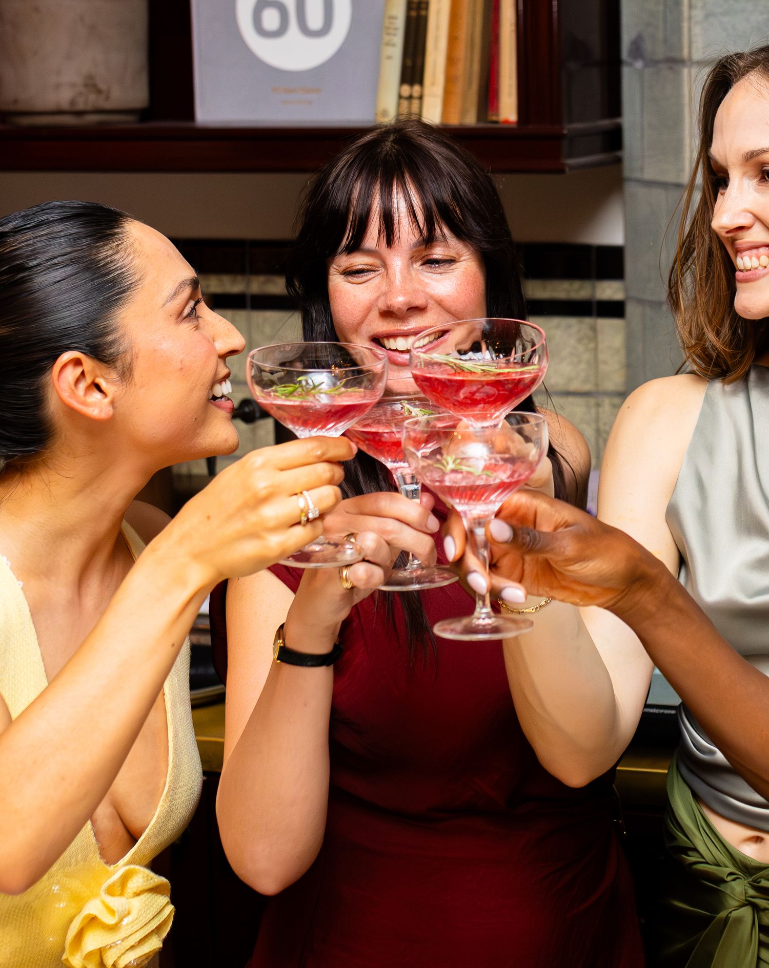 Friends toasting with pink cocktails in coupe glasses at a celebratory gathering.