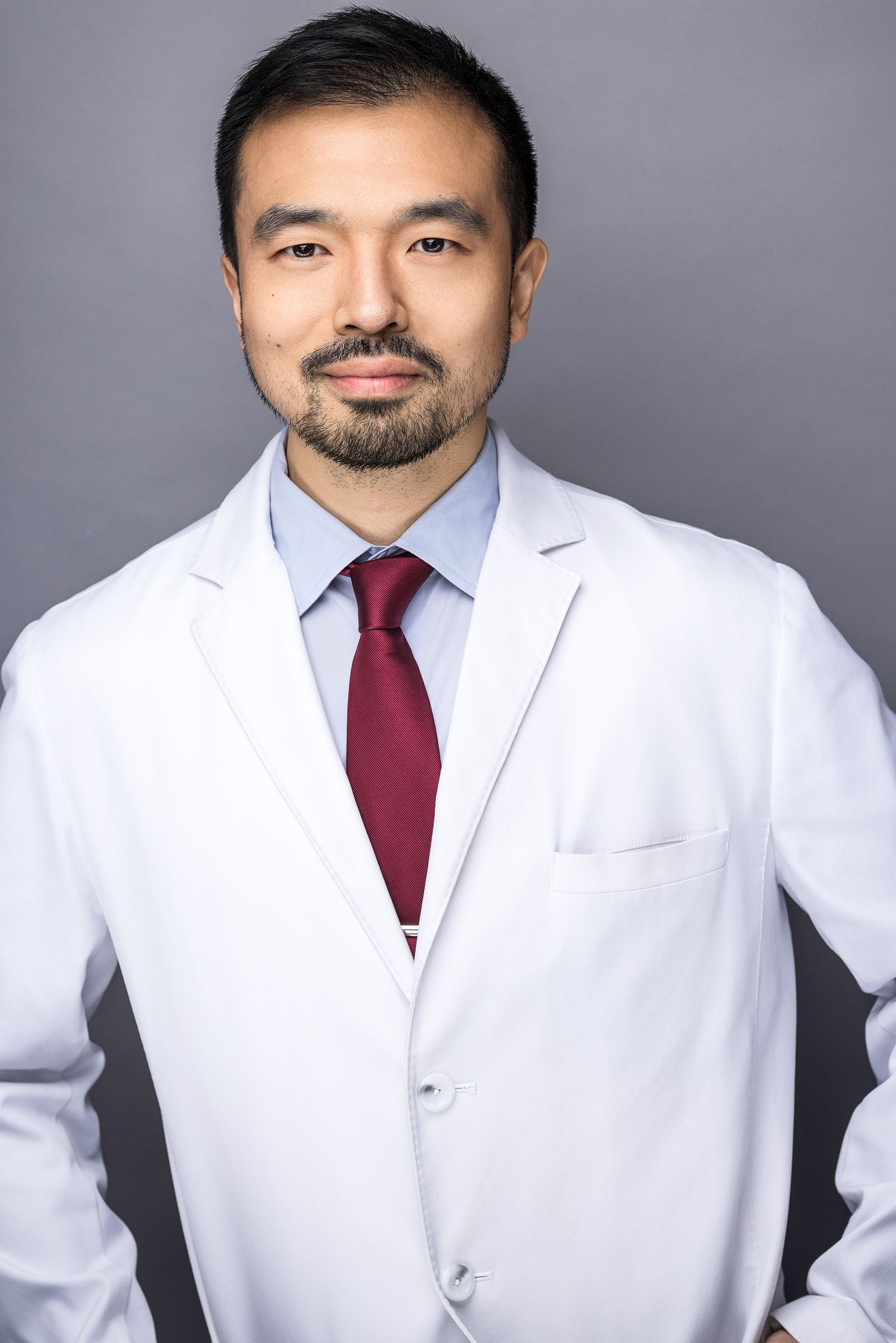 Male doctor in a white coat, blue shirt and tie, in a professional medical headshot. Taken in a Beacon, NY, studio.