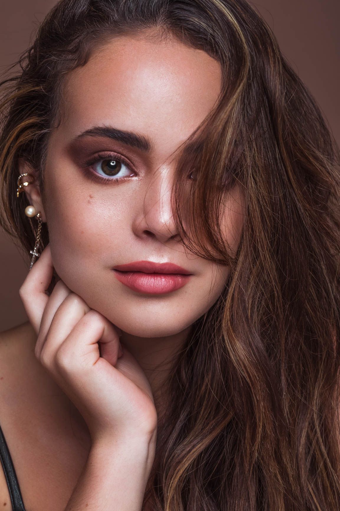 Young brunette woman with gold ear cuff and natural makeup poses for a beauty portrait.