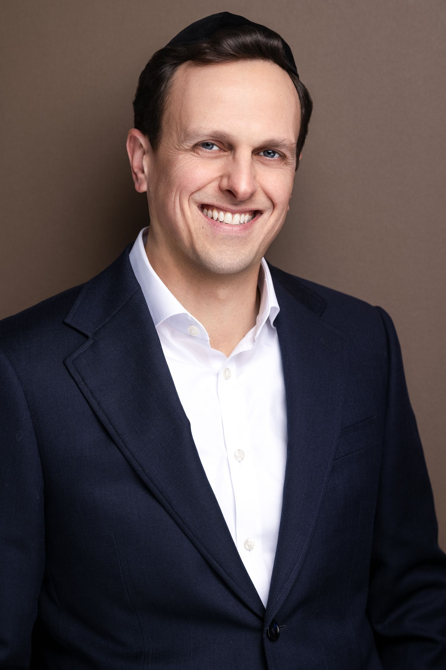 Smiling man in navy blazer and white shirt poses for professional business headshot.