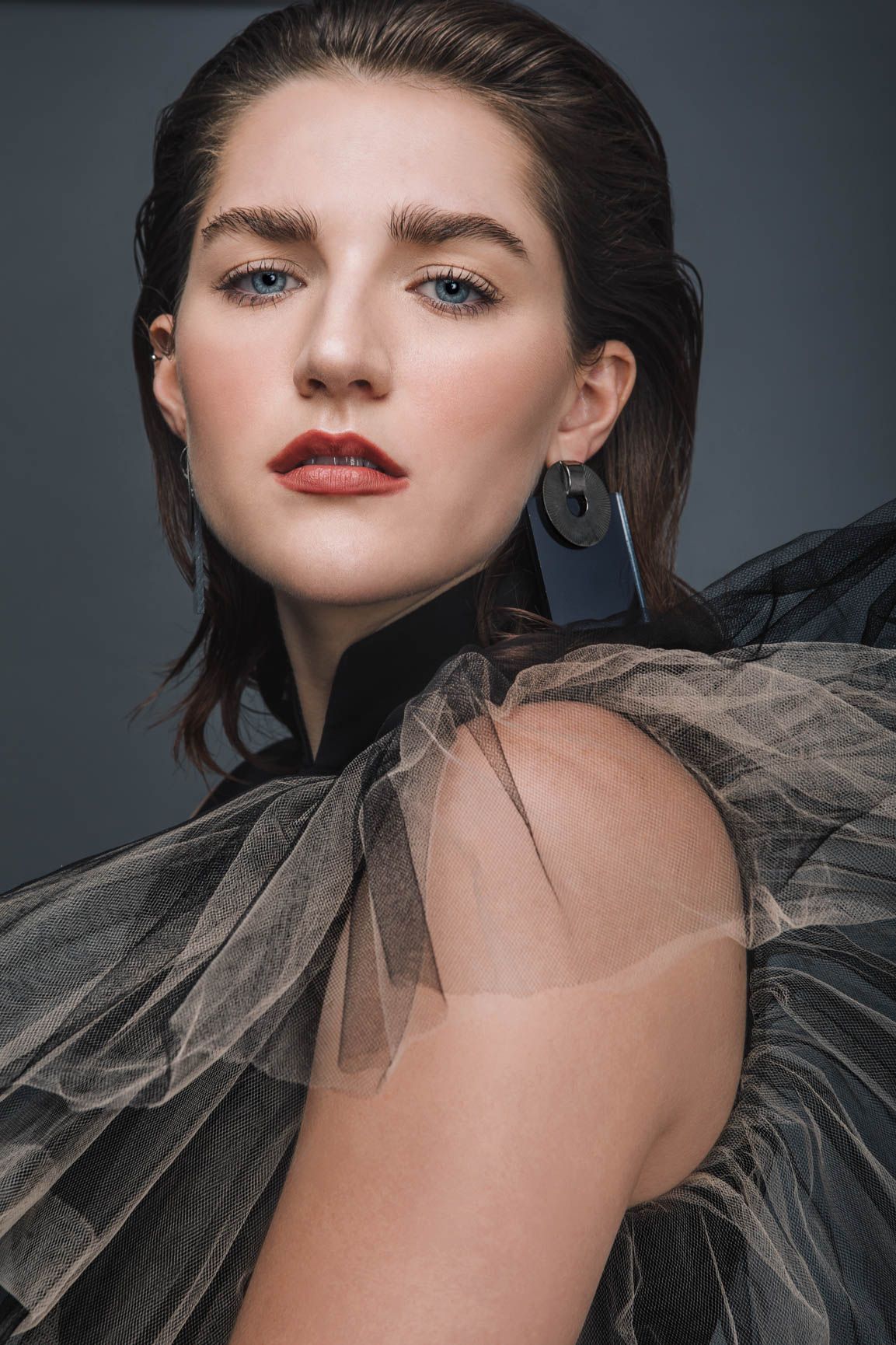 Elegant young woman with blue eyes wearing a dramatic black tulle gown poses for a high-fashion editorial portrait.