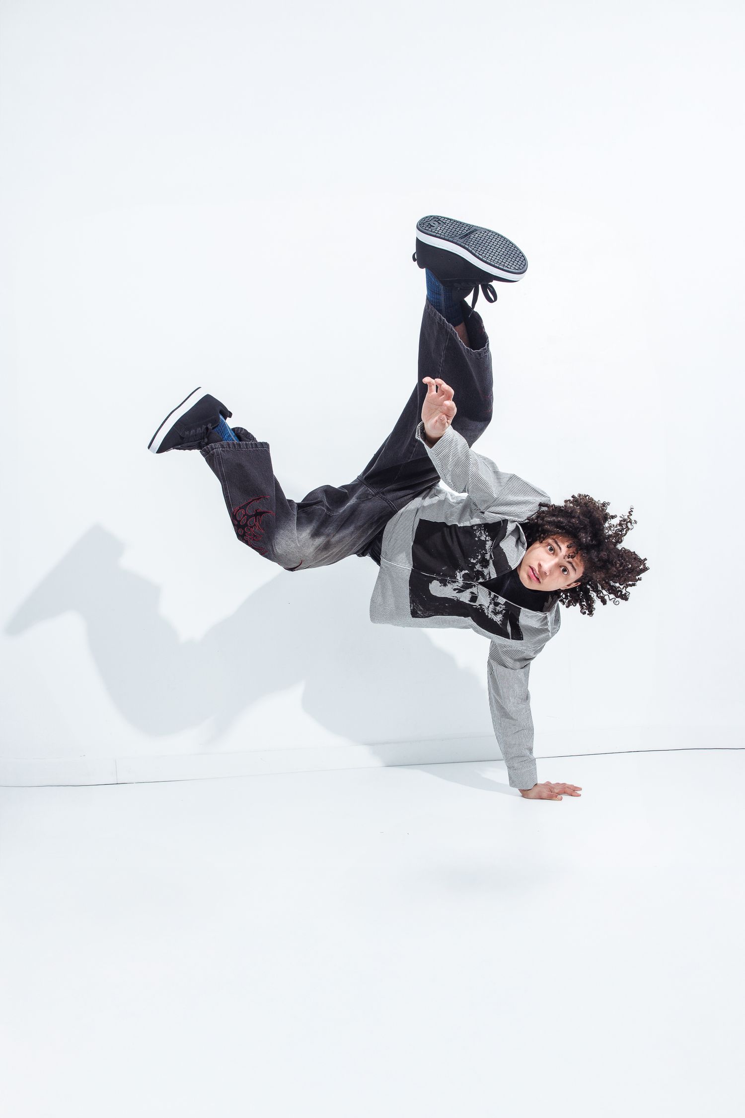 Breakdancer performing a one-handed freeze move with legs in the air on a white background.