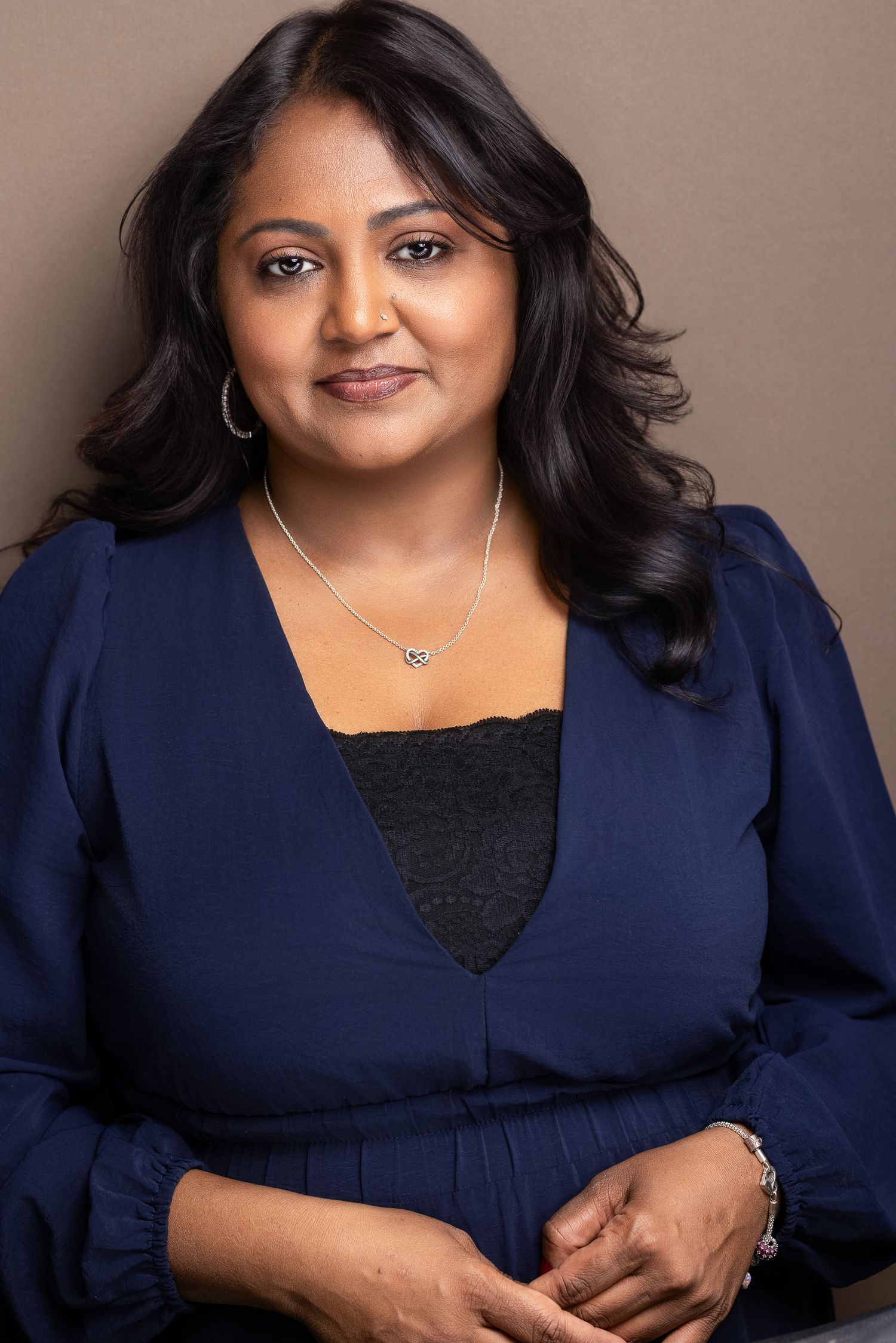 Professional portrait of a woman in a navy blue blouse wearing a silver necklace, smiling confidently.