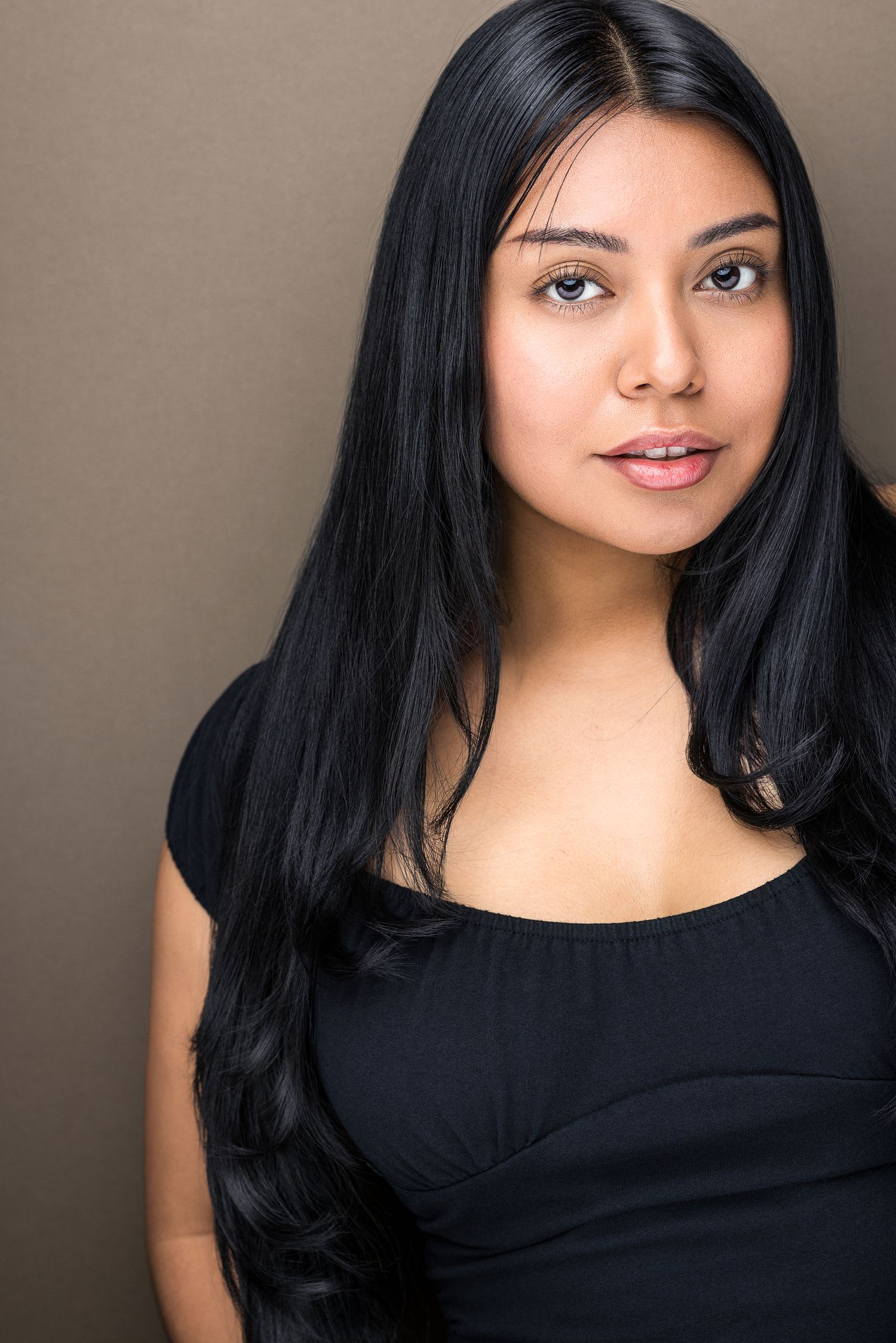 Young woman with long black hair wearing a black top against a brown background.