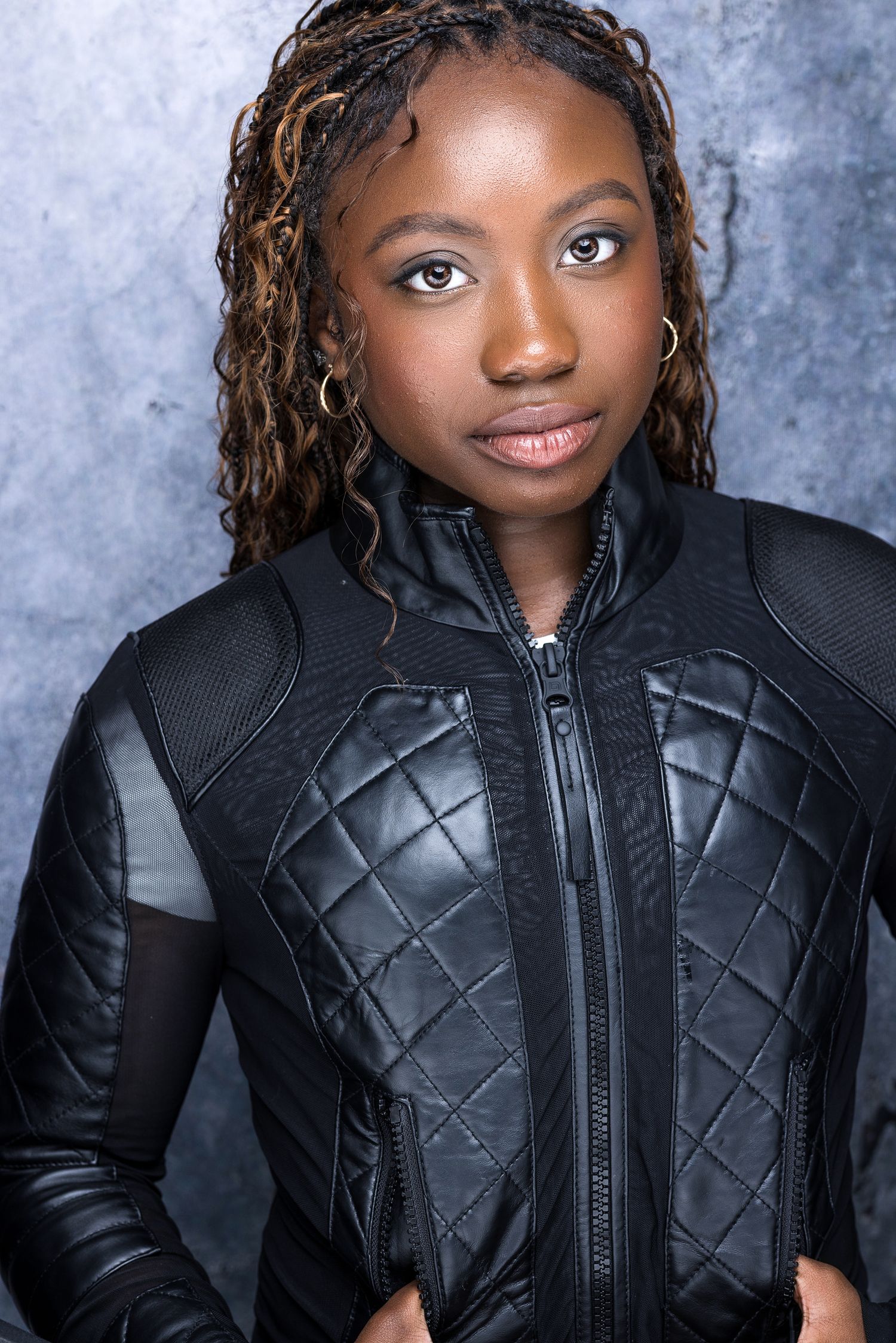 Young Black woman with braided hair wearing quilted black leather jacket poses for dramatic professional headshot.