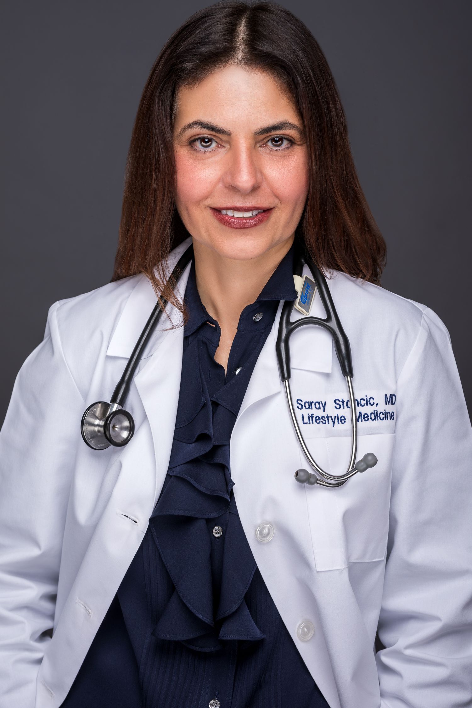 Female doctor in white lab coat with stethoscope, name tag reads Saray Stancic MD Lifestyle Medicine.