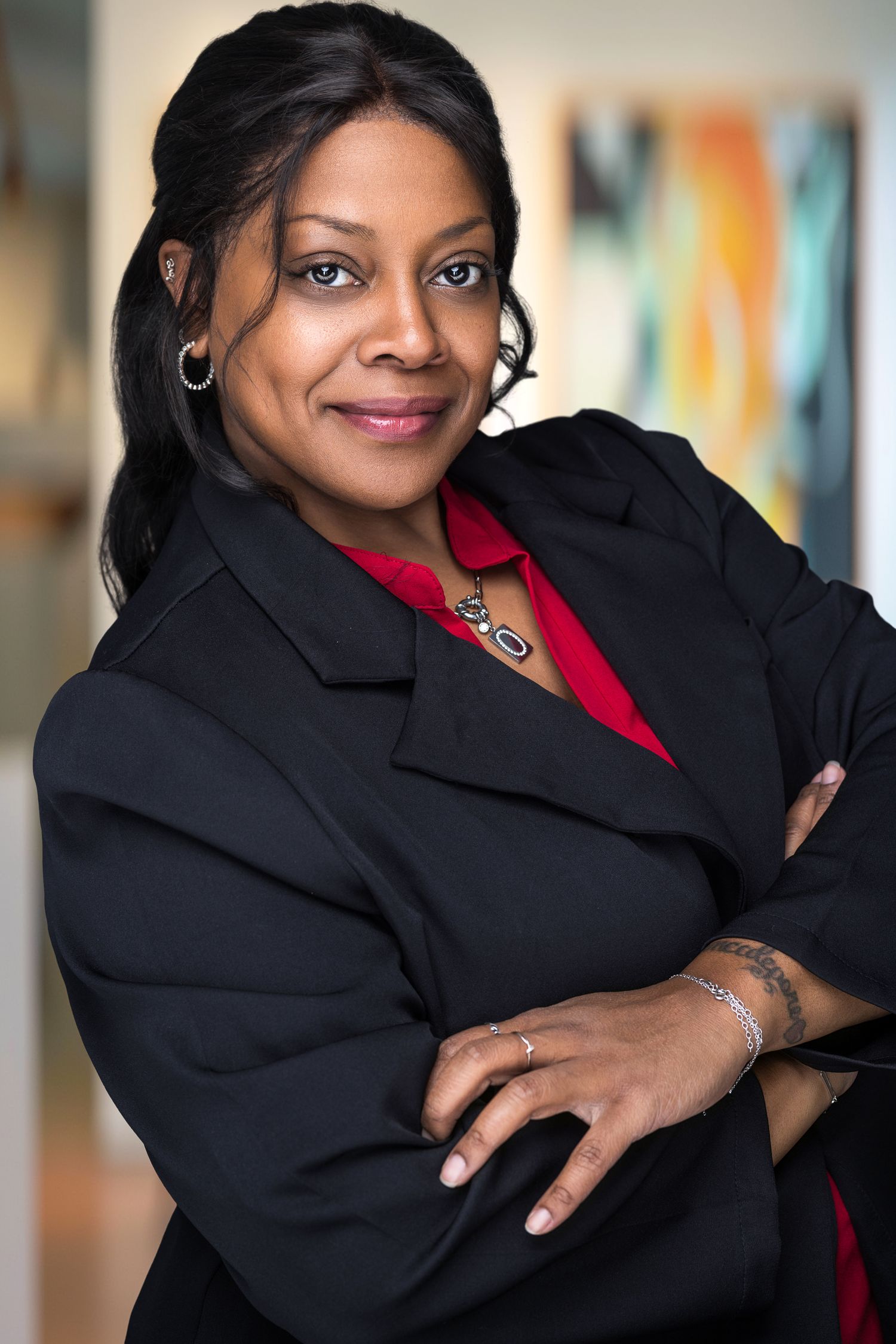 Professional Black woman in black blazer and red blouse poses with arms crossed.