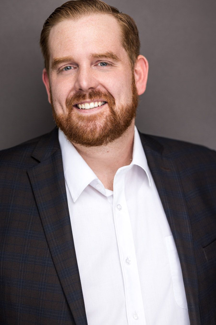 Portrait of man with sept-back hair wears a dark plaid blazer over a white open-collar shirt in Beacon, NY.
