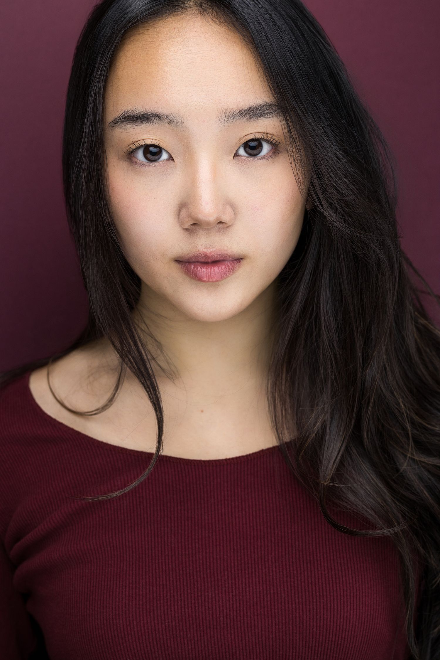 Young Asian woman with long dark hair wearing a burgundy top poses for a professional headshot.