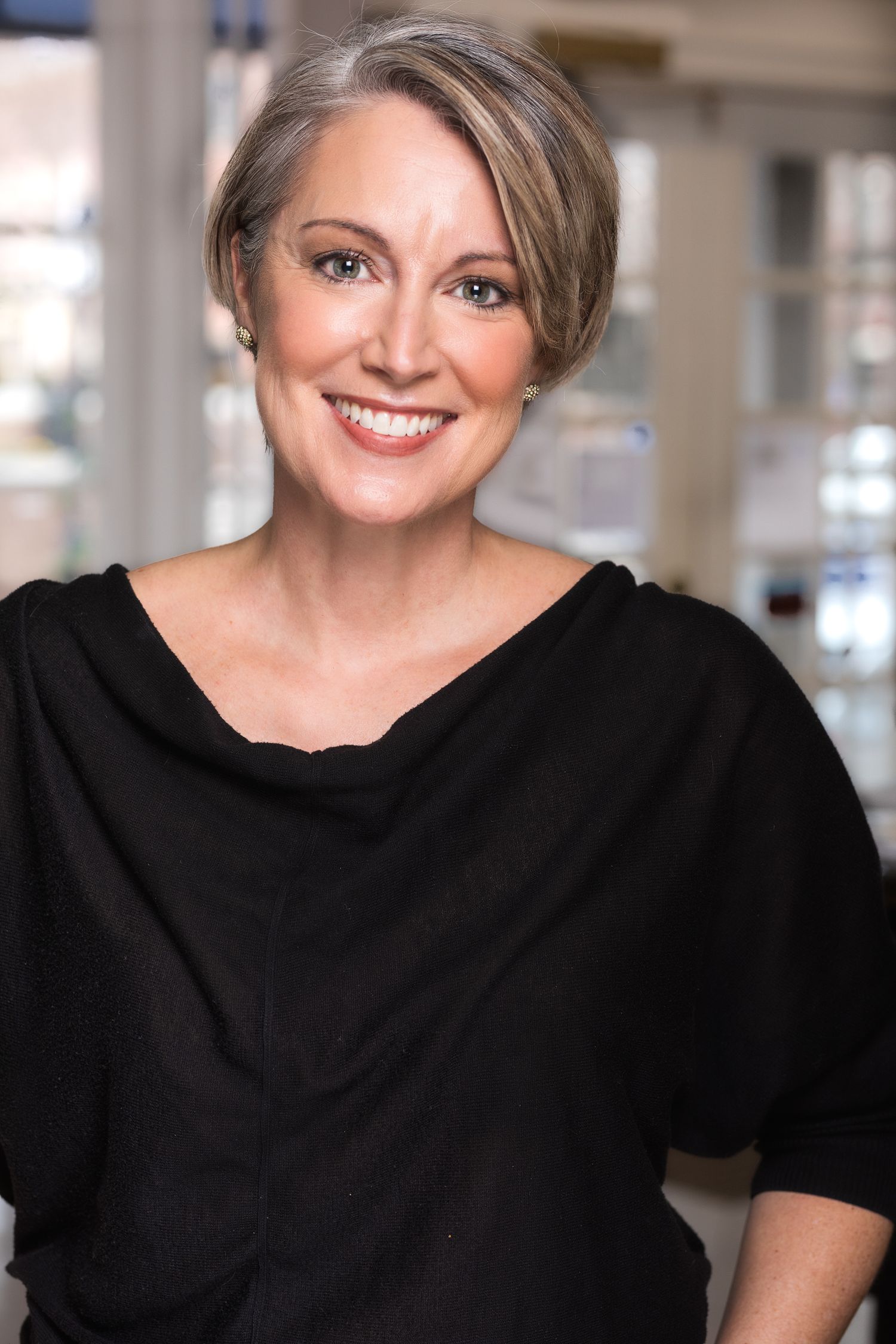 Smiling middle-aged woman with short gray hair wearing a black top in a bright interior.