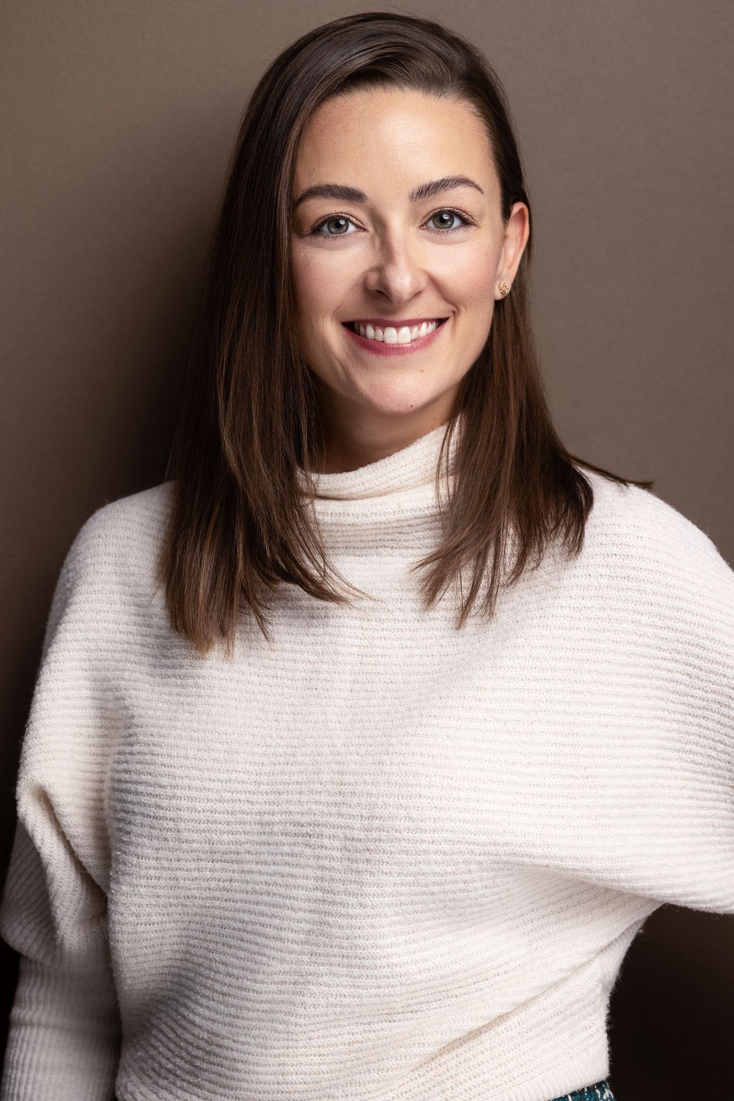 Smiling woman with brown hair wearing a white turtleneck sweater poses for a professional headshot photo.