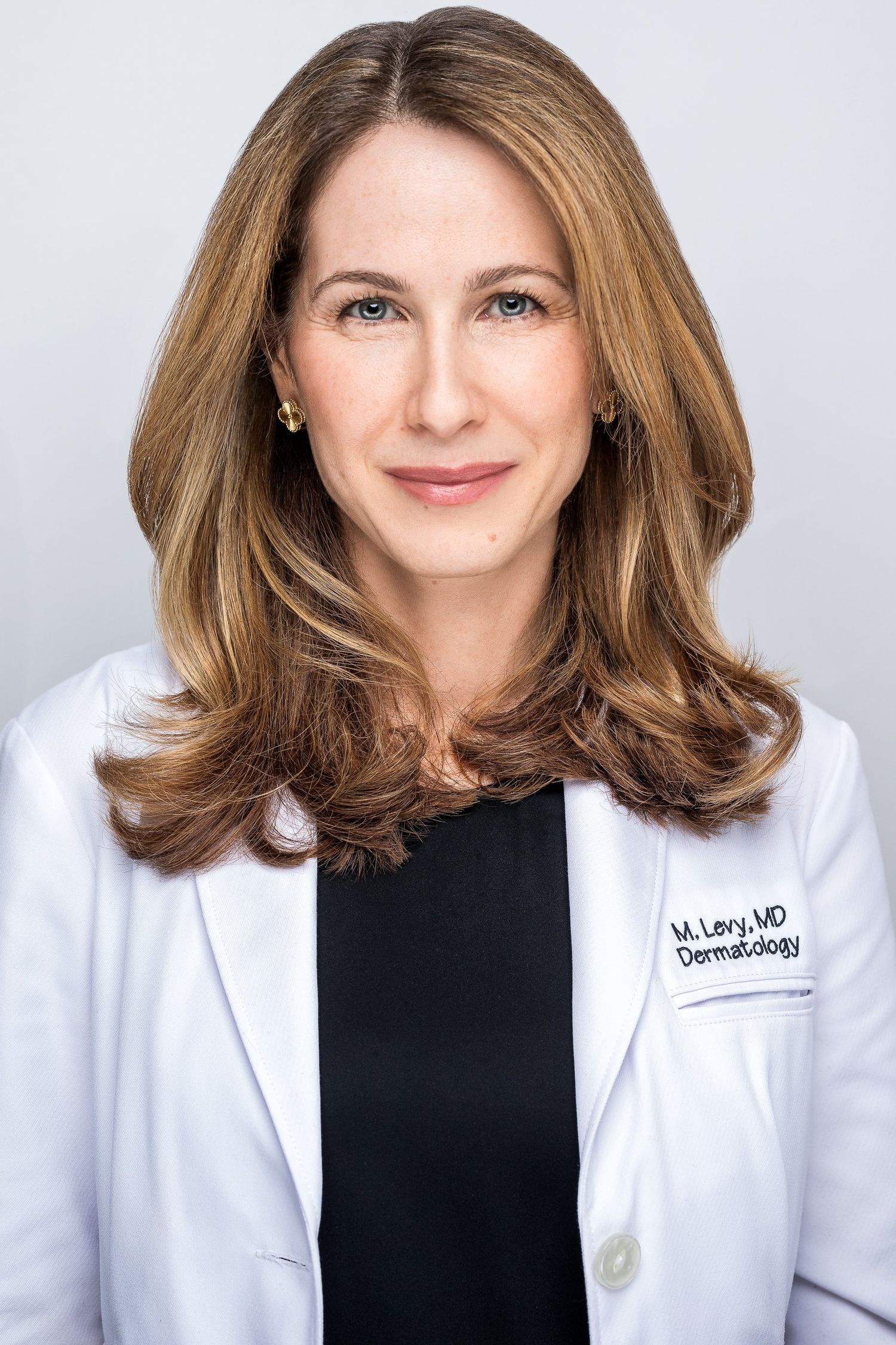 Dermatologist M. Levy, MD, in a white lab coat, smiling professionally against a gray background in Hudson Valley, NY.