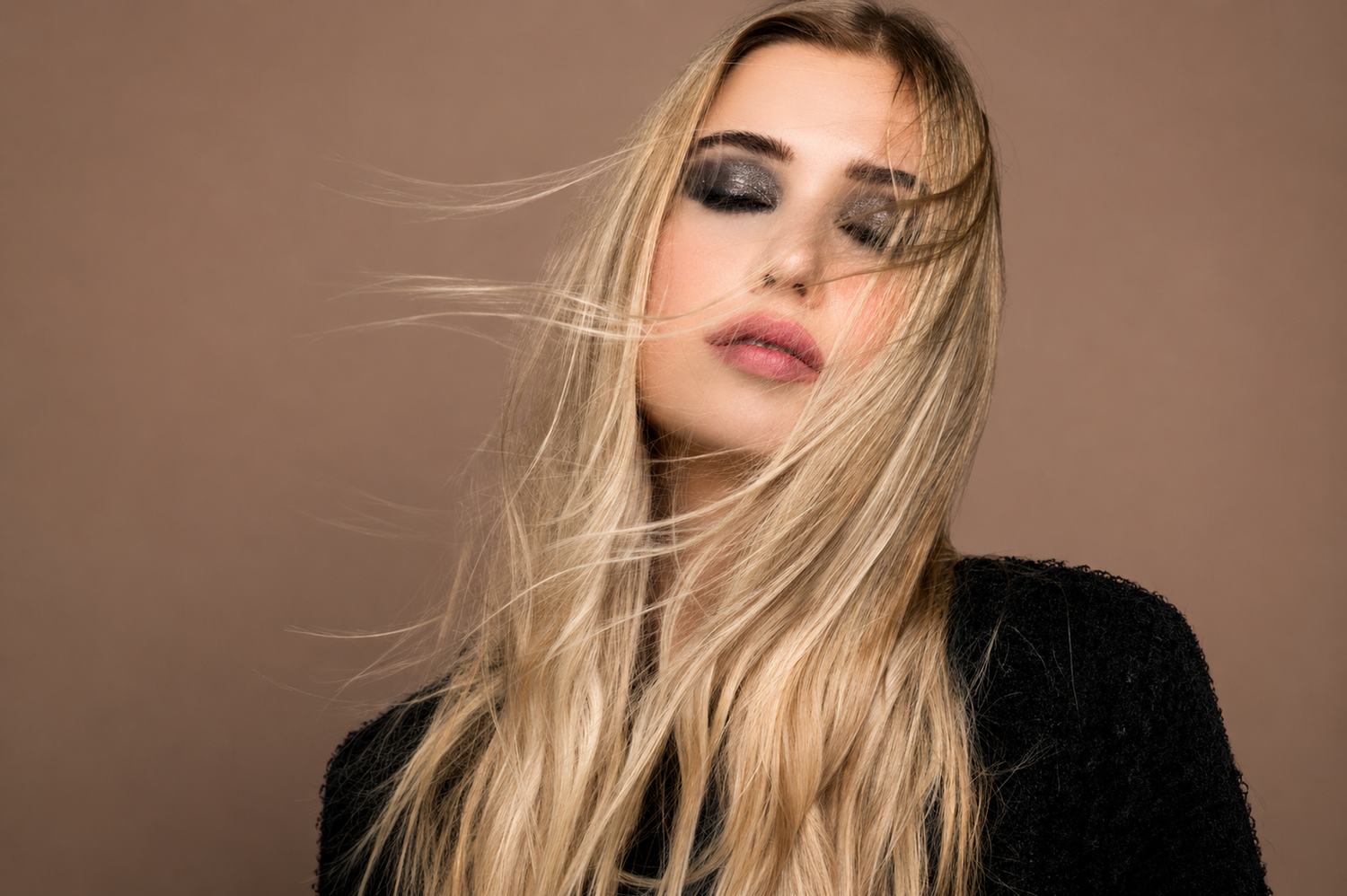 Woman with windswept blonde hair and smoky eye makeup poses dramatically in a black sparkly top.