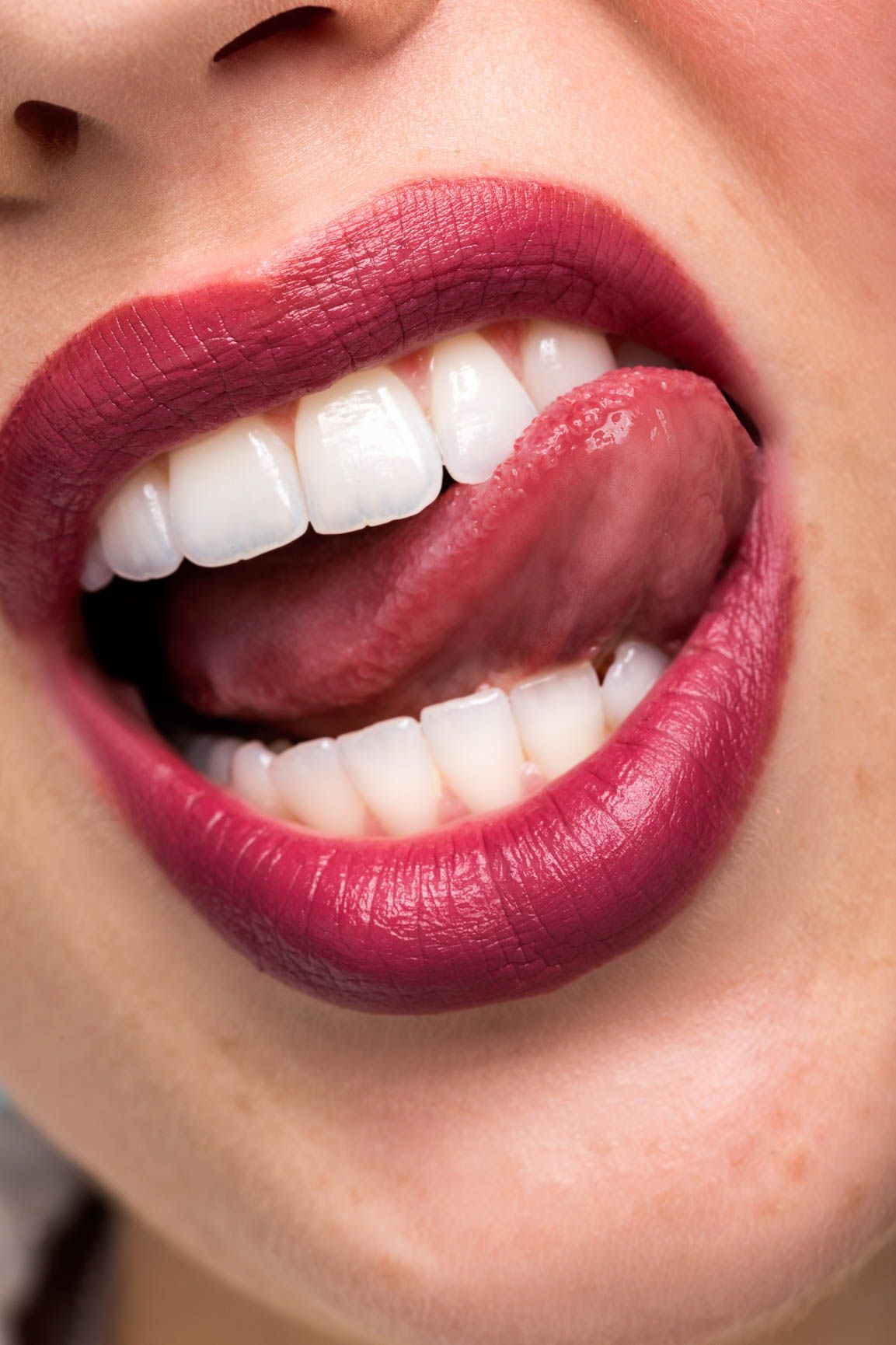Close-up of woman's open mouth with red lipstick and tongue touching upper teeth.
