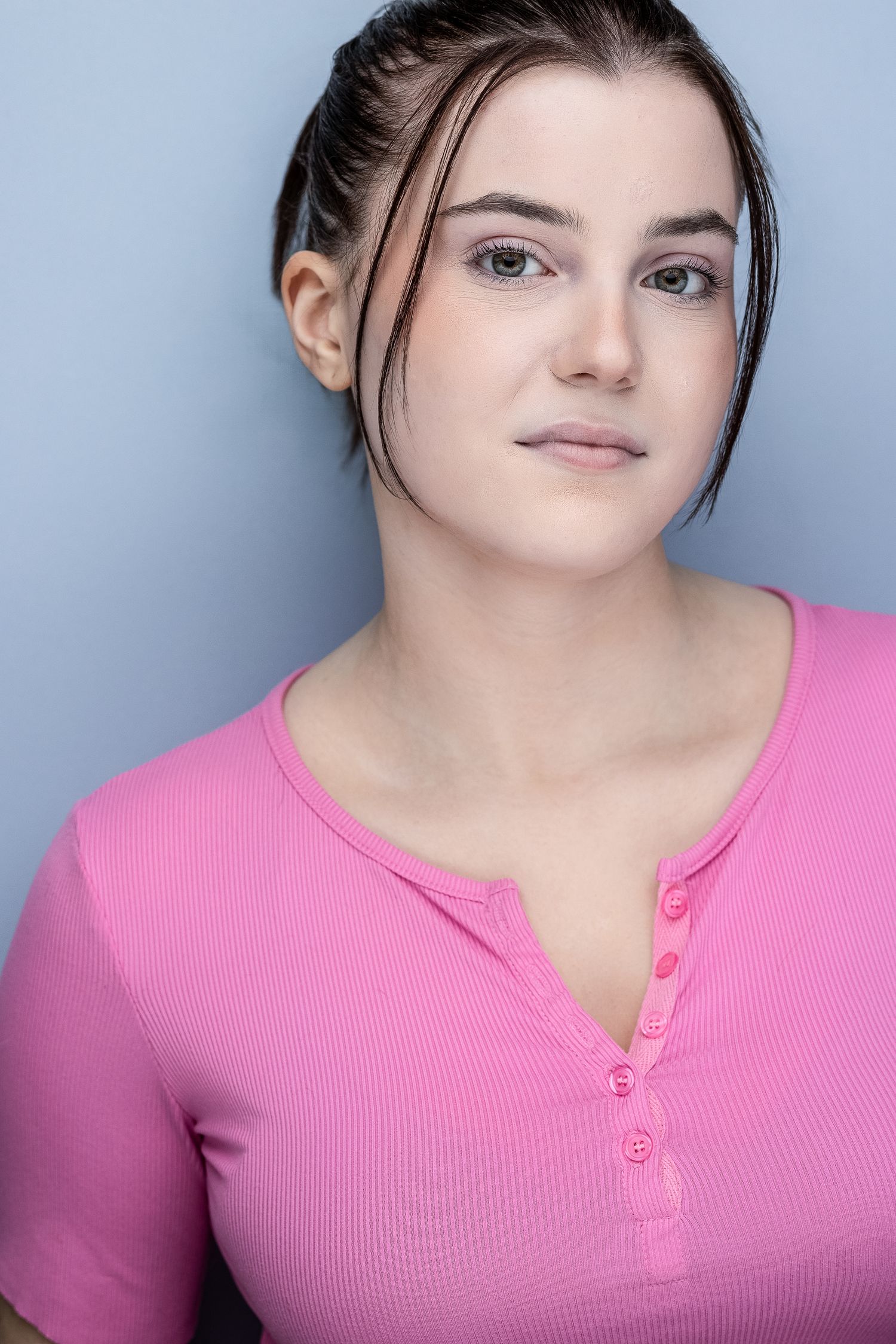 Young woman with pulled-back dark hair wearing a pink ribbed top poses for a professional headshot.