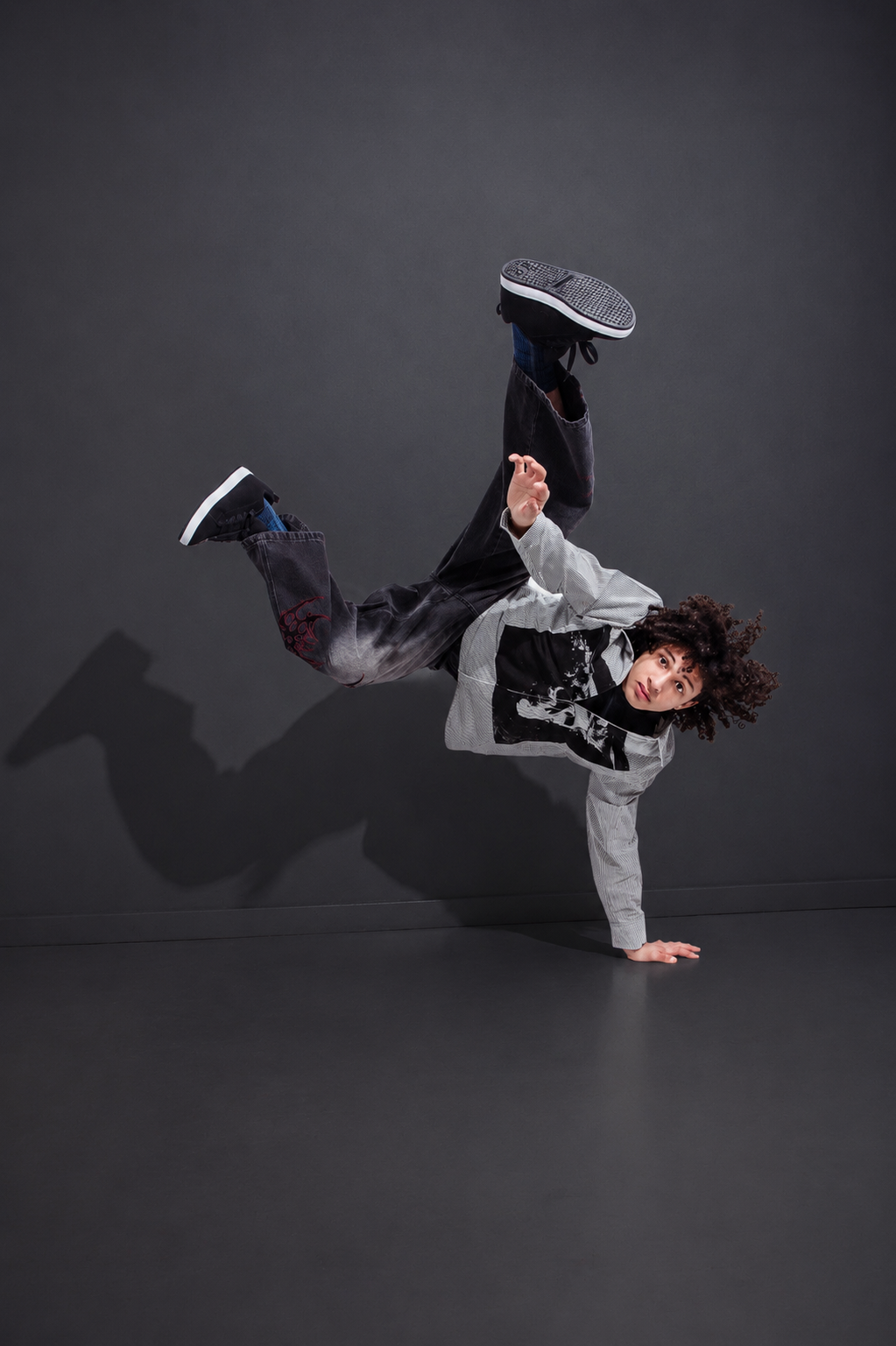 Male breakdancer executes an impressive one-handed freeze pose against a dark gray studio background.