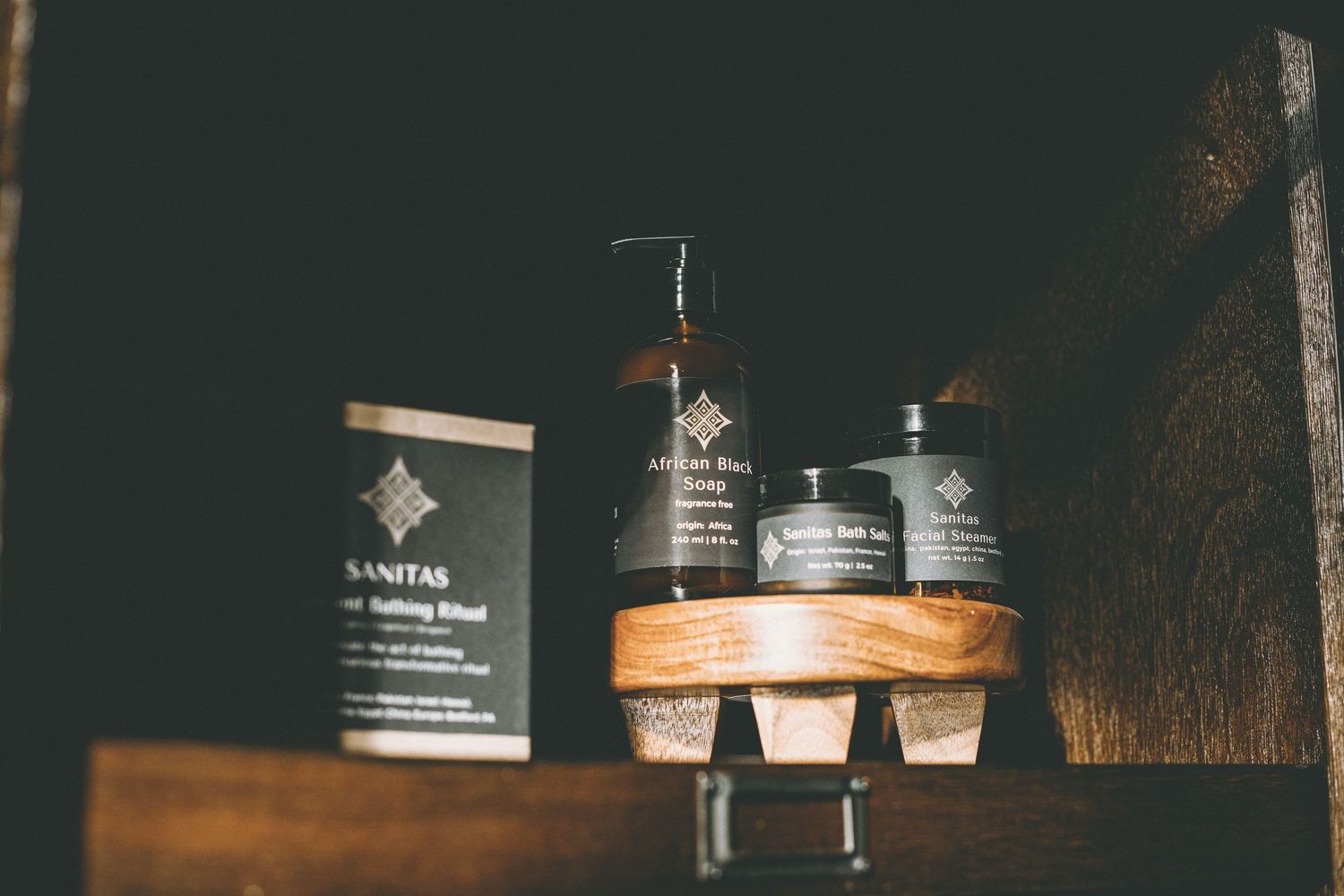 Wooden shelf displaying Sanitas natural skincare products, including a boxed item, a pump bottle and two jars.