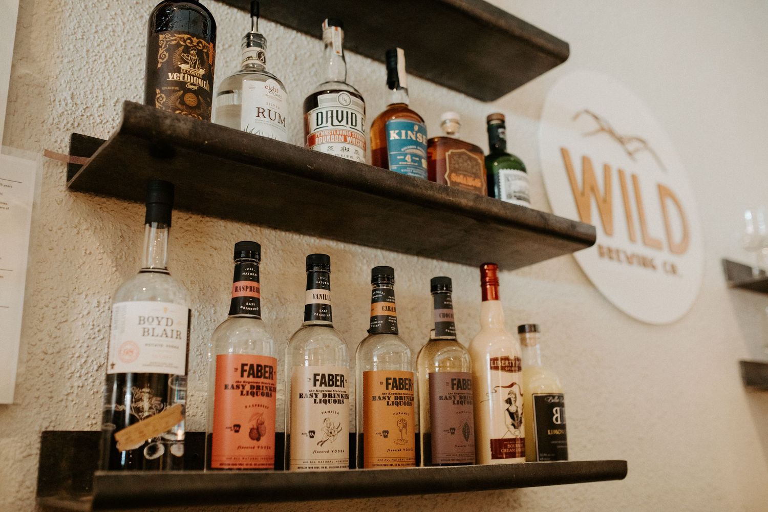 Wall shelves of whiskey and liquor bottles beside a Wild Brewing Co. sign in a taproom.