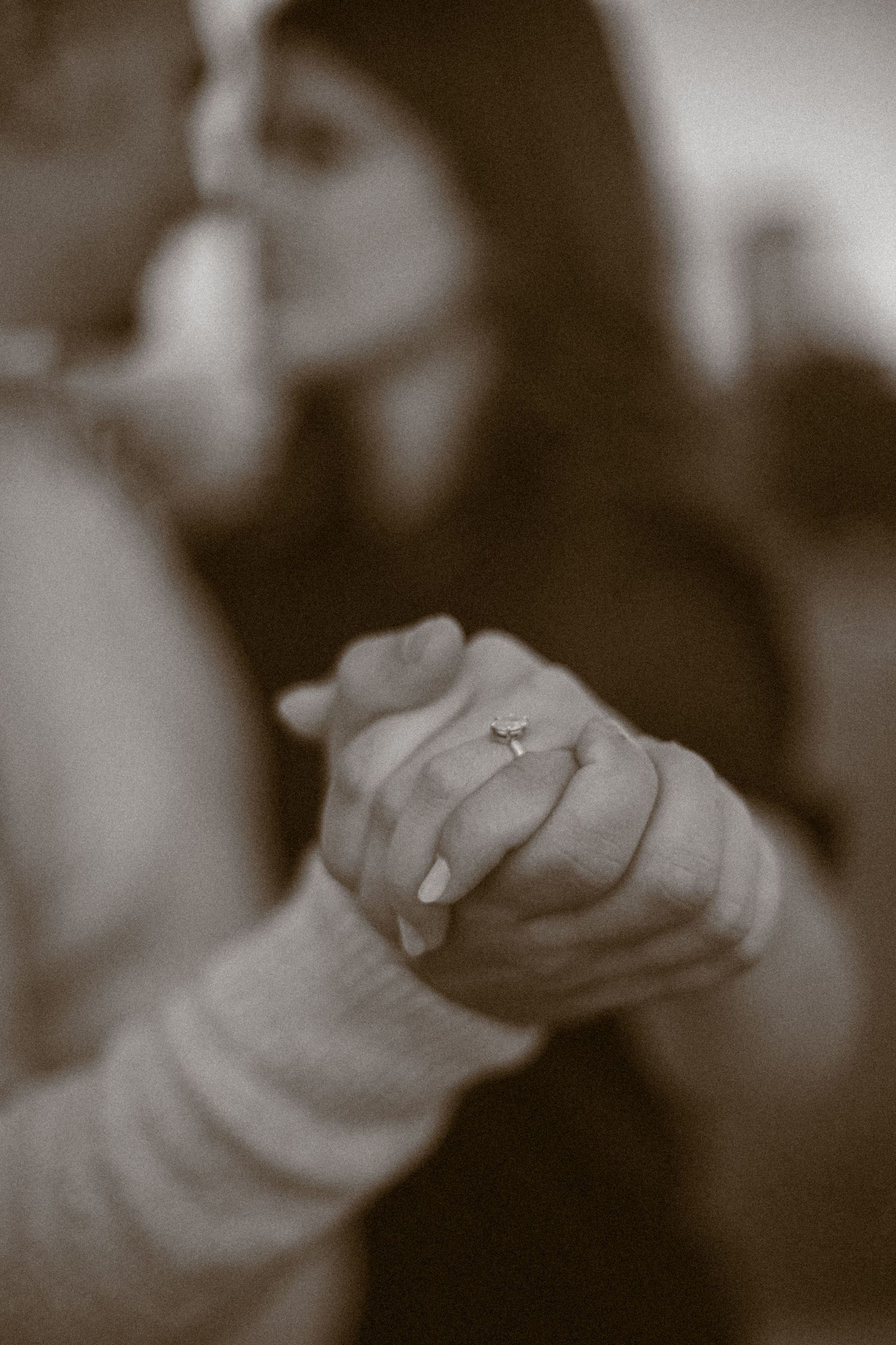 Close-up sepia photo of a couple holding hands, showing an engagement ring on the woman's finger.