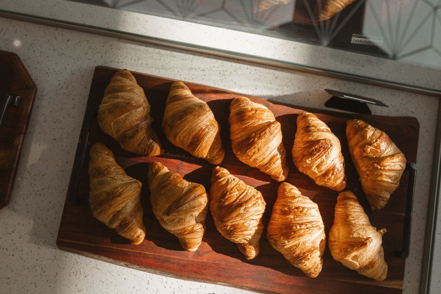 Overhead view of nine freshly baked golden croissants arranged on a dark wooden serving board.