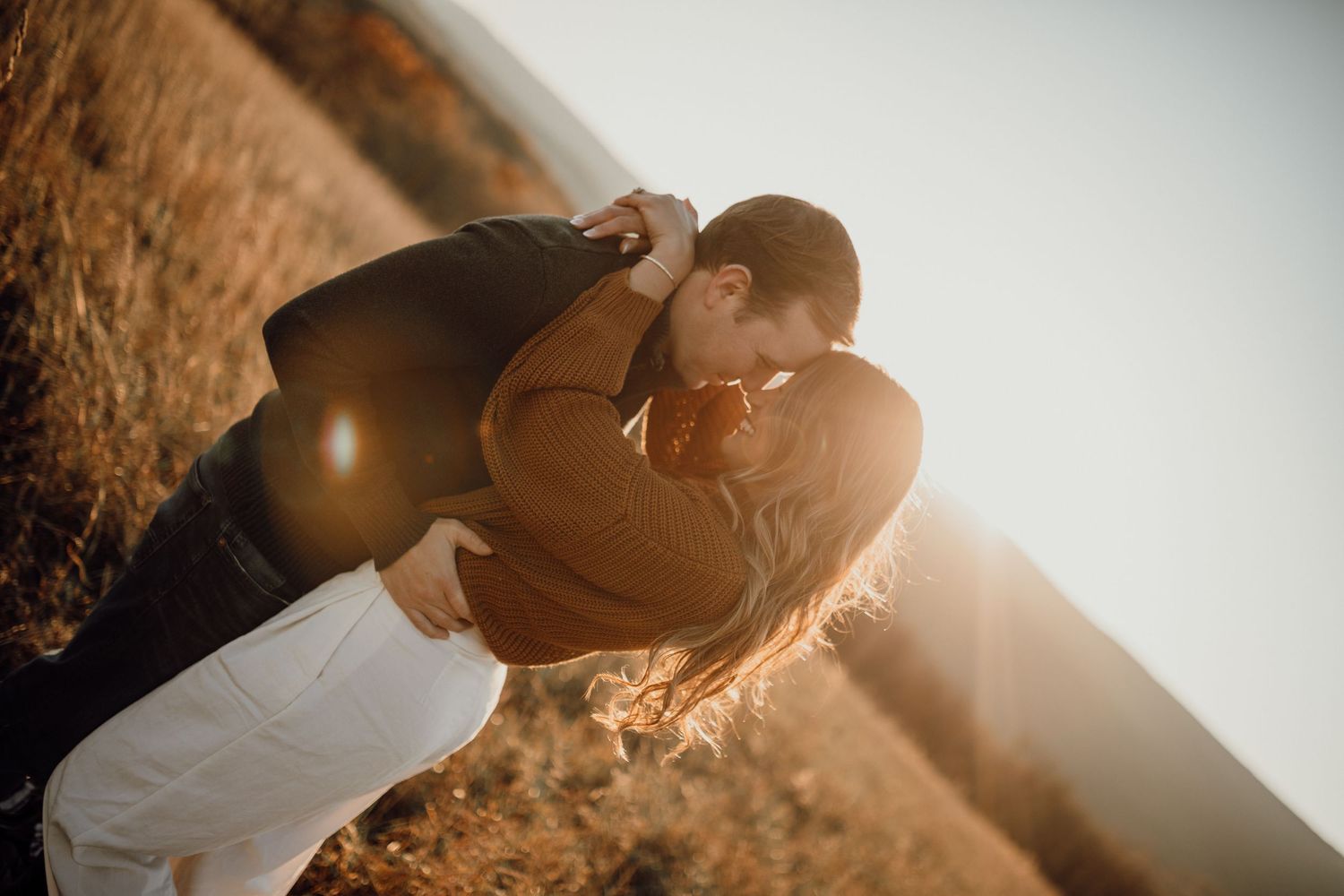 Couple sharing a romantic kiss in warm golden sunlight during an outdoor engagement session.