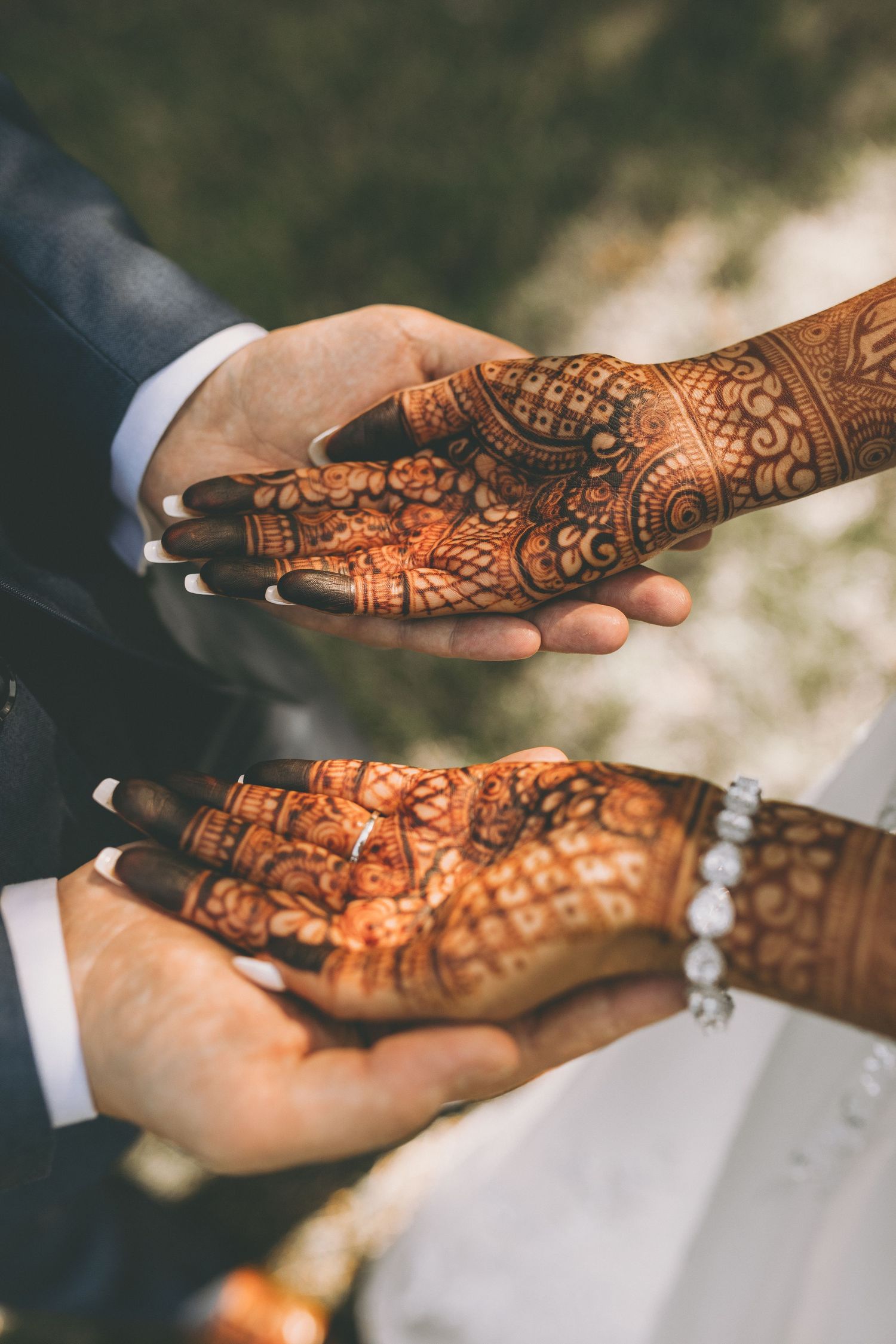 Bride's intricate henna-covered hands rest in the groom's hands in an overhead view of a traditional wedding mehndi design.