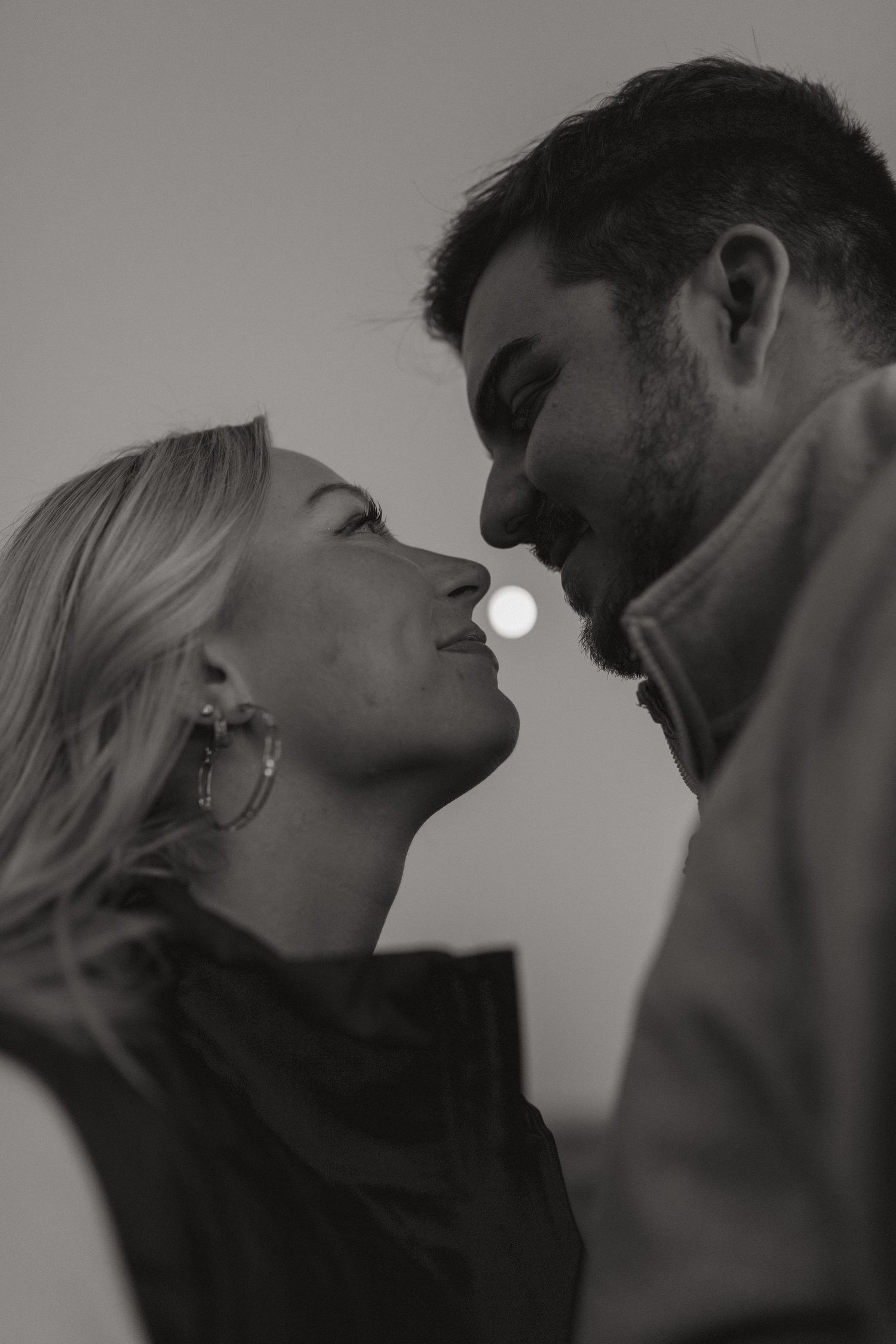 Black and white portrait of a couple nose to nose in a tender moment, with the moon glowing softly behind them.