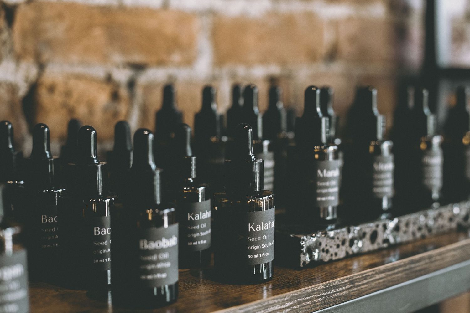 Rows of dark apothecary dropper bottles labeled Baobab lined up on a rustic wooden shelf against a brick wall.