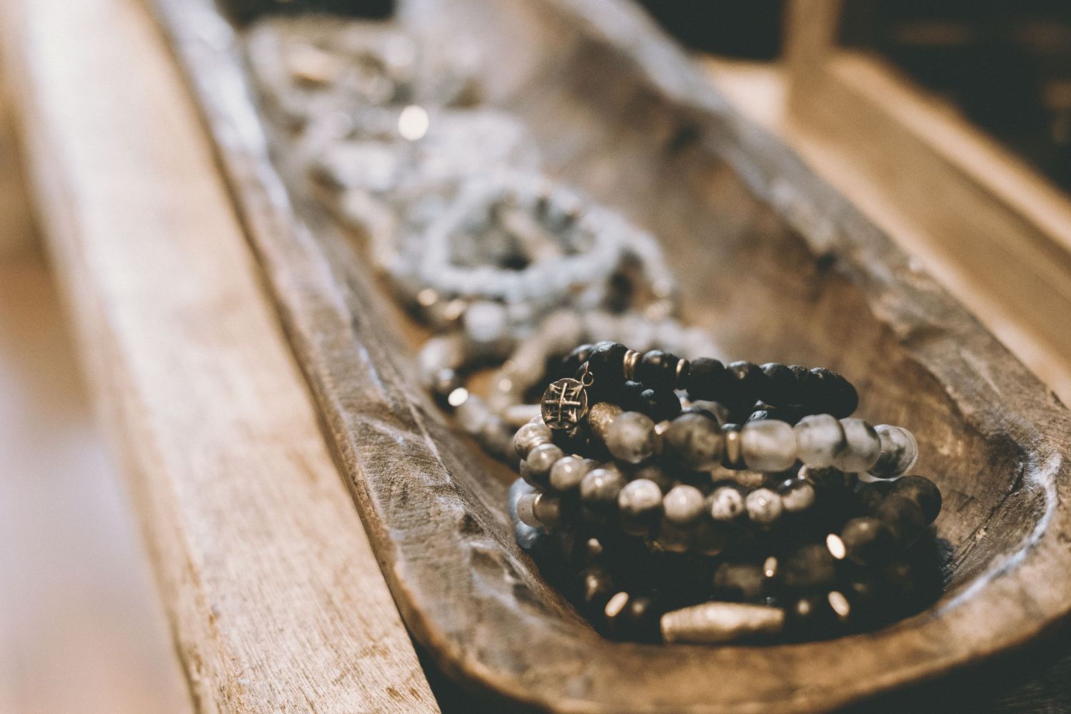 Wooden tray holding beaded bracelets and necklaces in black, white and silver tones.