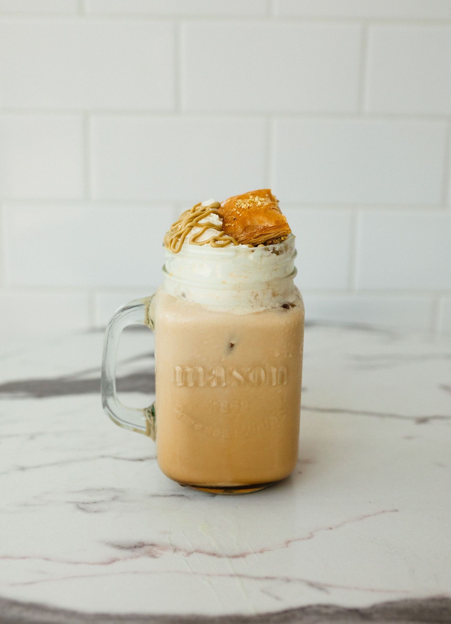 Iced caramel coffee in a mason jar mug topped with whipped cream, caramel drizzle and a cookie piece on marble.