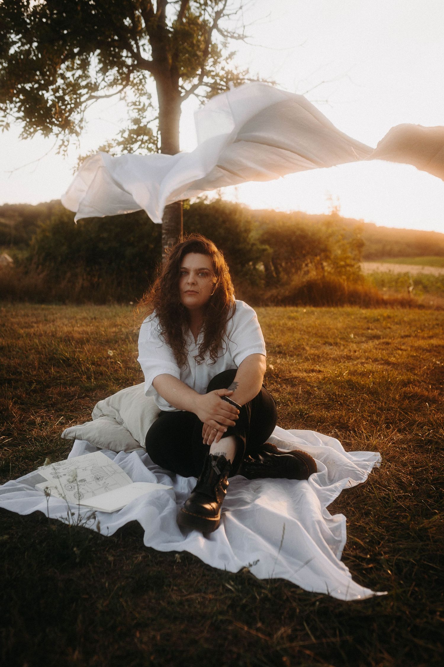 femme assise au sol sur un drap, qui pose sur l'herbe, voile au vent derrière elle