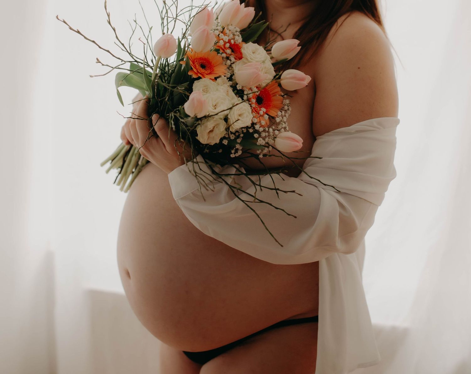 femme enceinte de profil, bouquet de fleur en main cachant sa poitrine