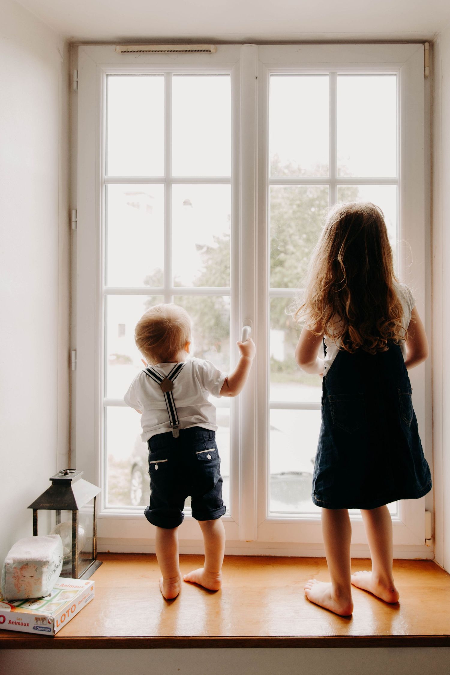 deux enfants, frère et soeur de dos, regardant par la fenêtre