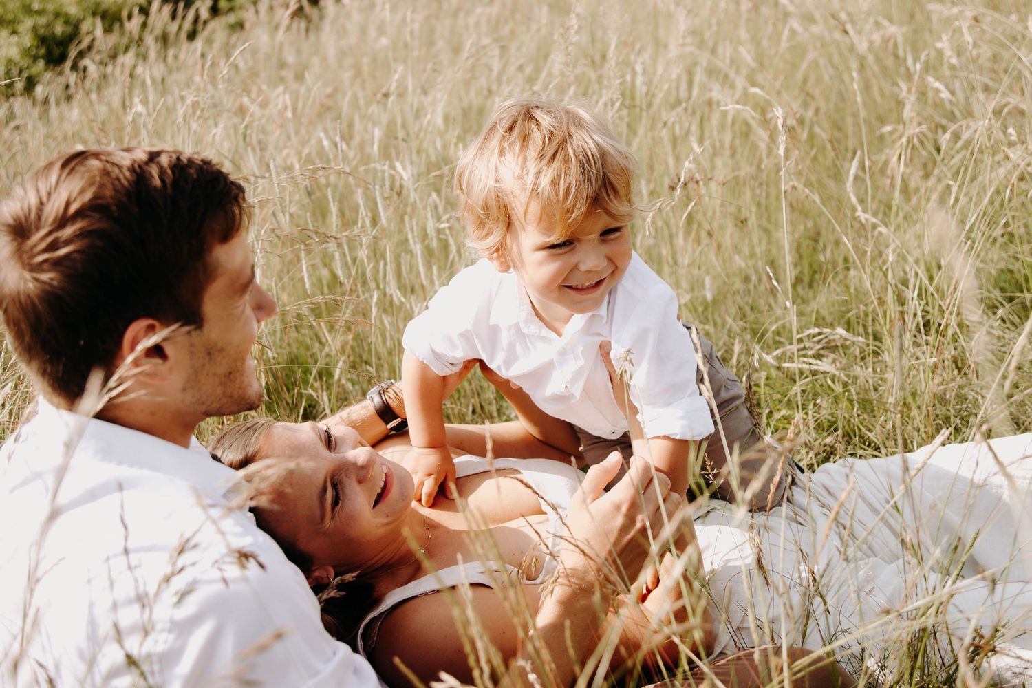 des parents et leur fils qui jouent, allongés dans l'herbe