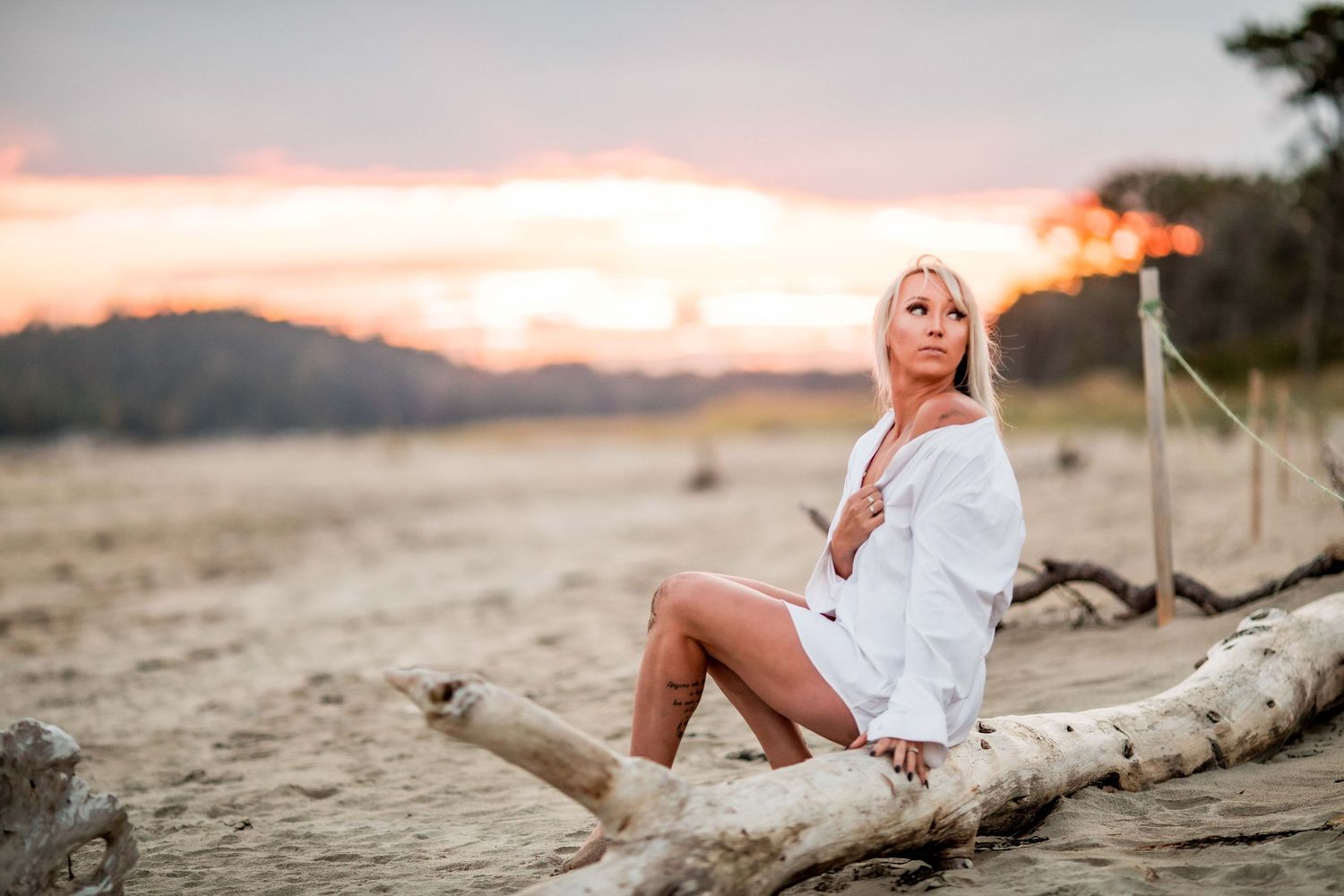 Blonde woman in white shirt sitting on driftwood at a beach during sunset Cape cod beach Boudoir photos