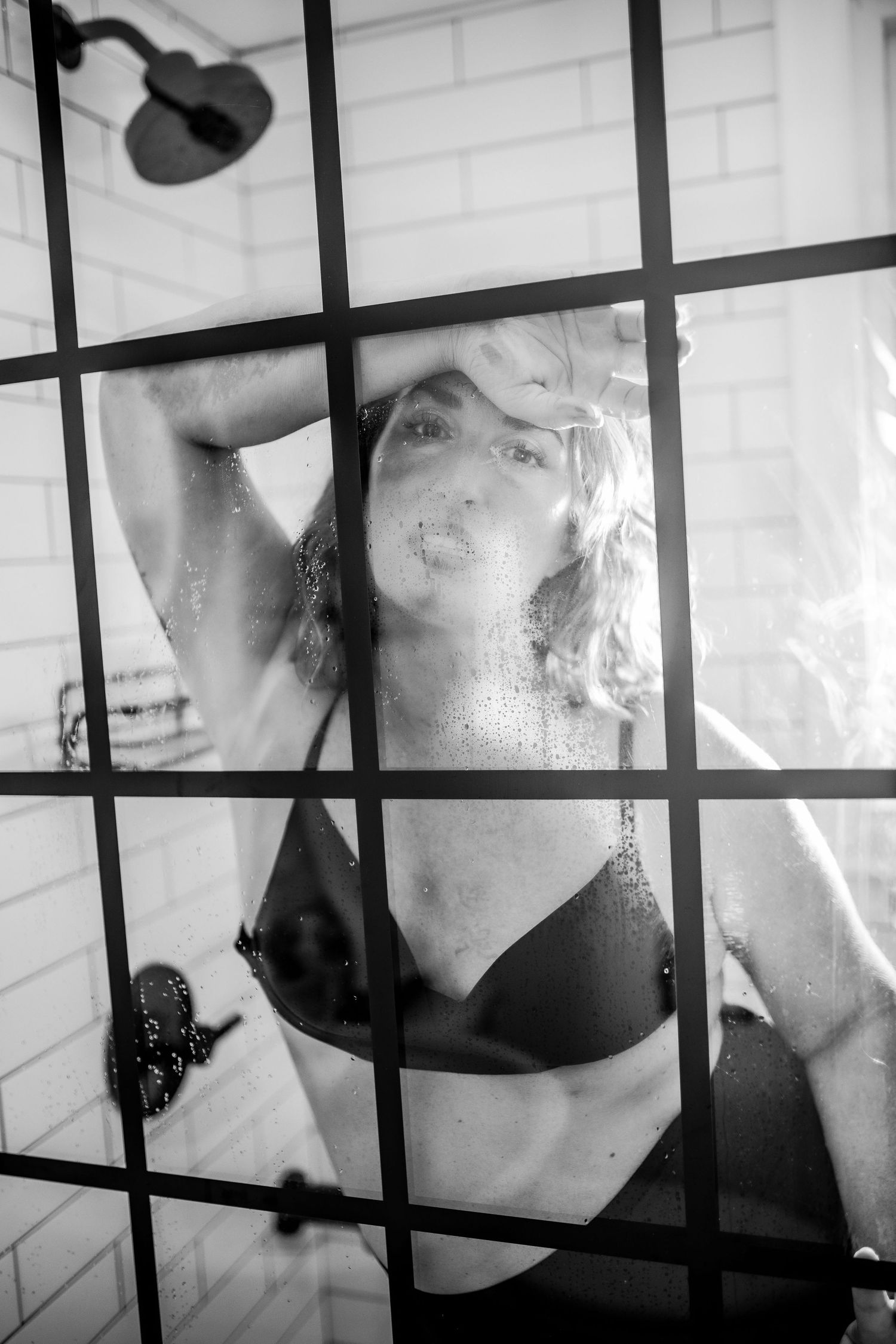 Black and white photo of woman in bikini top posing behind wet glass shower door Cape cod studio Boudoir photos