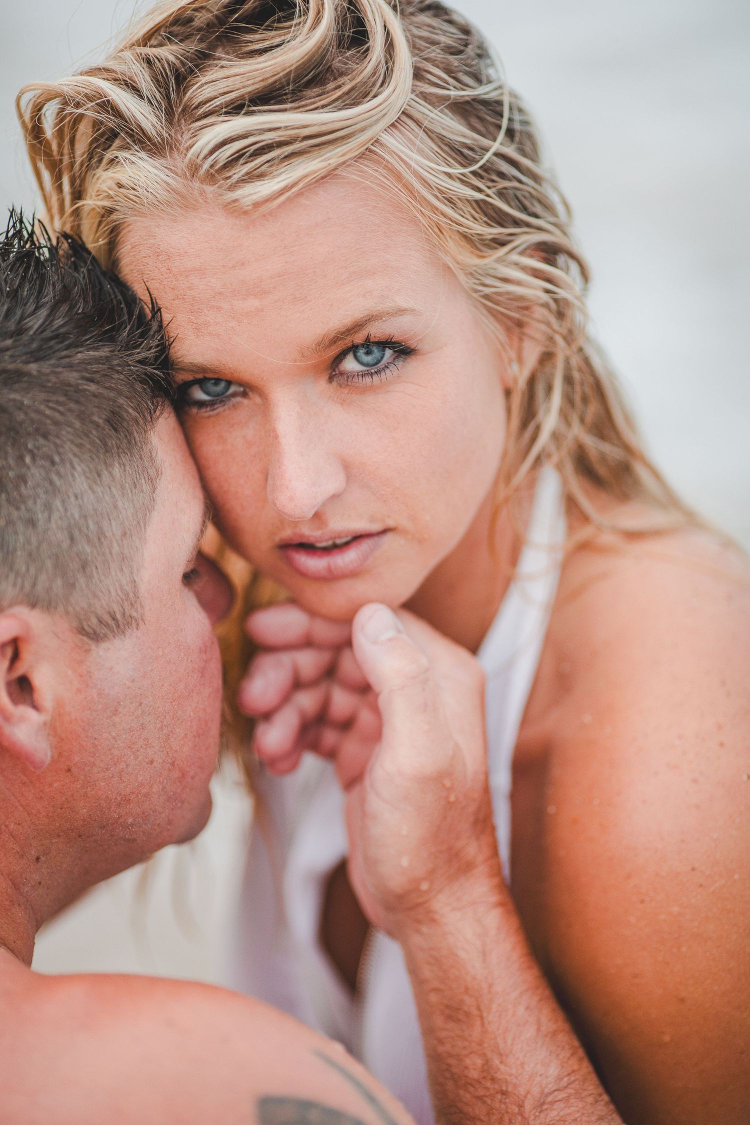 Close-up of a blue-eyed blonde woman gazing intensely while embracing her partner on the beach Cape cod couples studio Boudoir photos