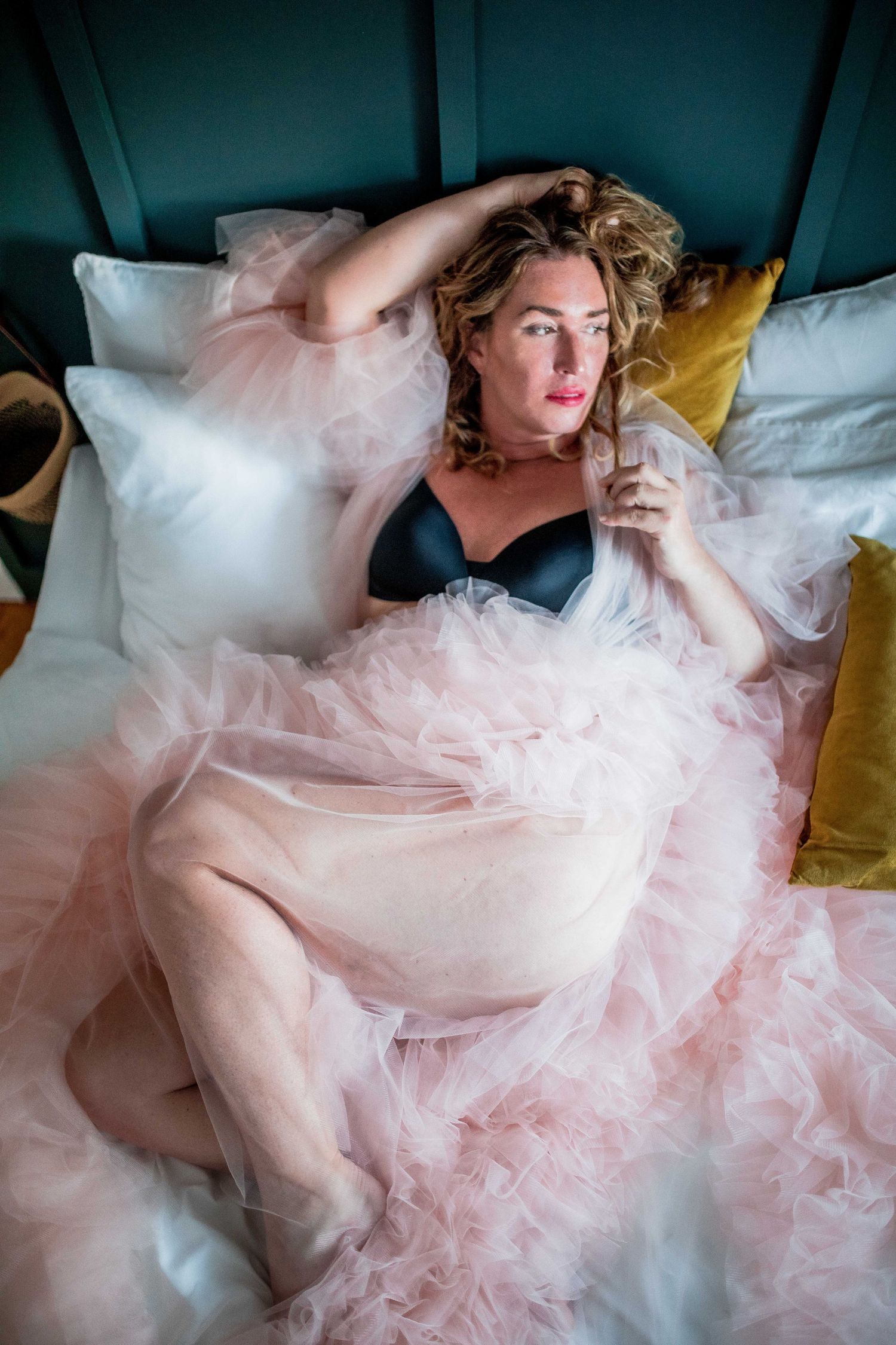 Woman in black bra and pink tulle skirt reclining on white bed with teal headboard. Cape cod studio Boudoir photos